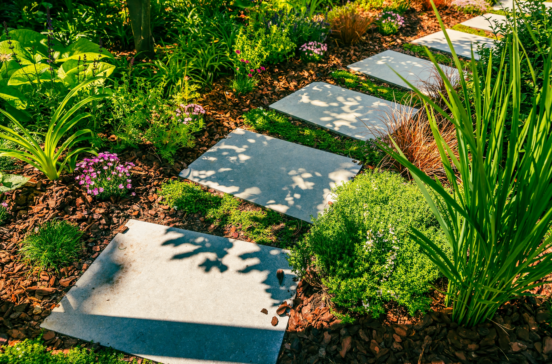 A stone walkway in a garden surrounded by plants and flowers.
