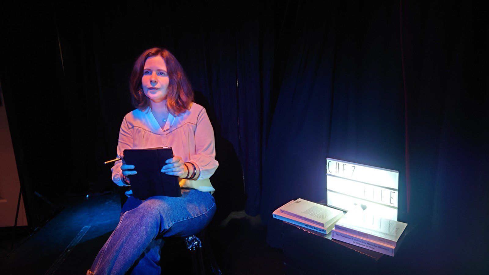 une femme est assise dans une pièce sombre, tenant une tablette.