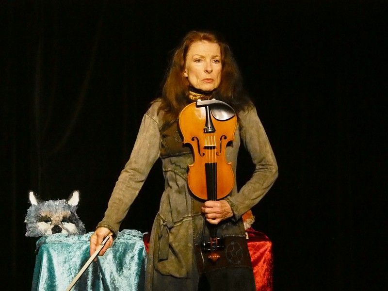 Une femme tient un violon devant un chat sur une scène.