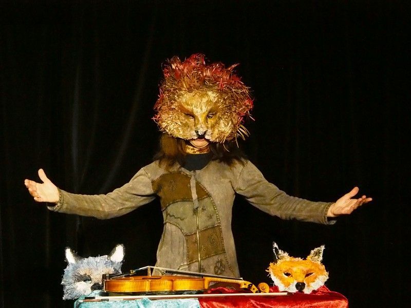 Une personne portant un masque de lion joue du violon sur une scène.