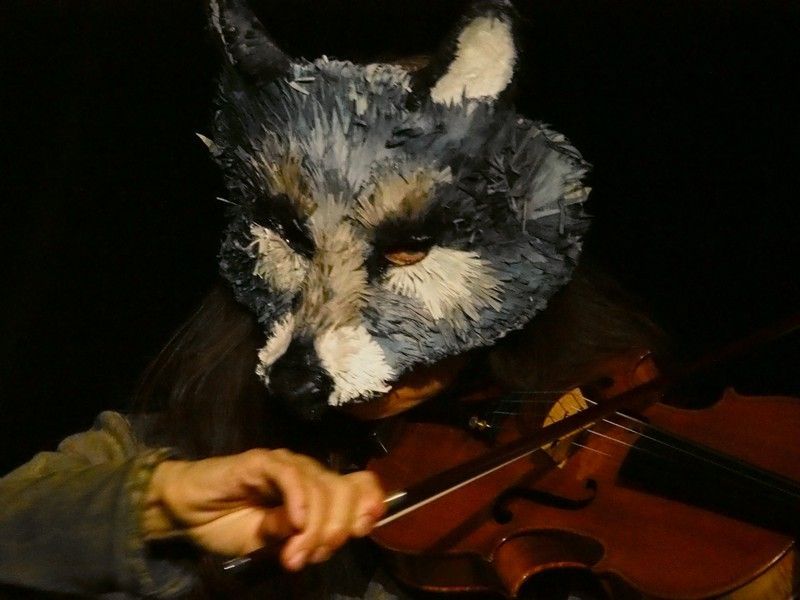 Une personne portant un masque de loup joue du violon