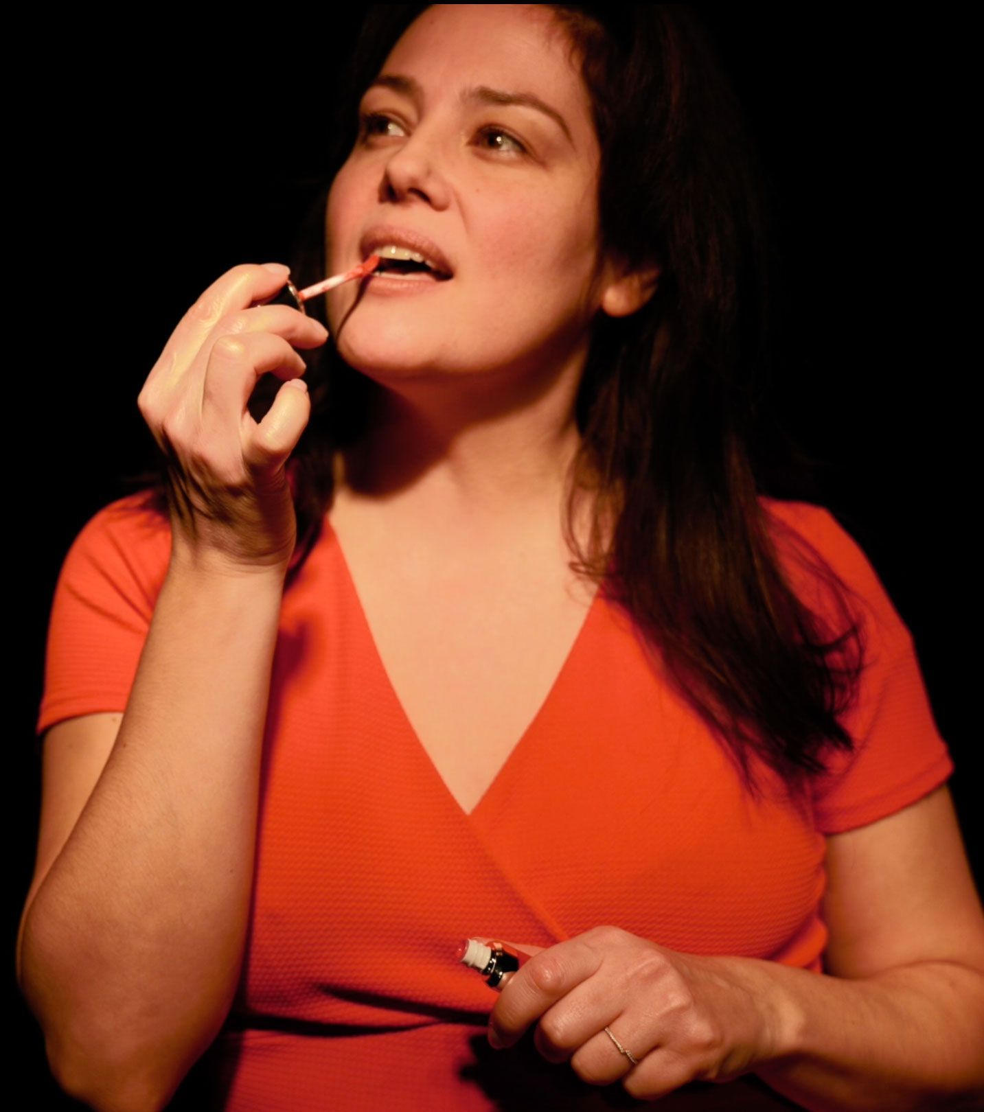 Une femme en chemise orange applique du rouge à lèvres