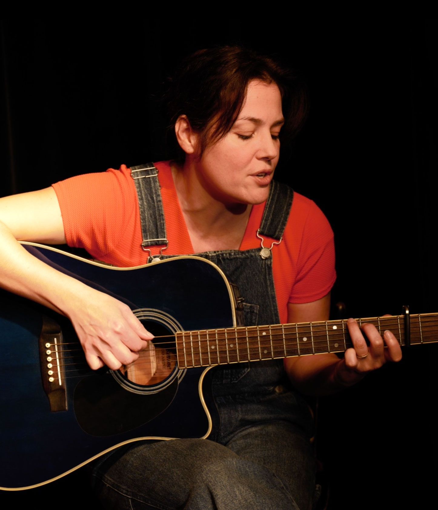 Une femme en salopette joue de la guitare bleue