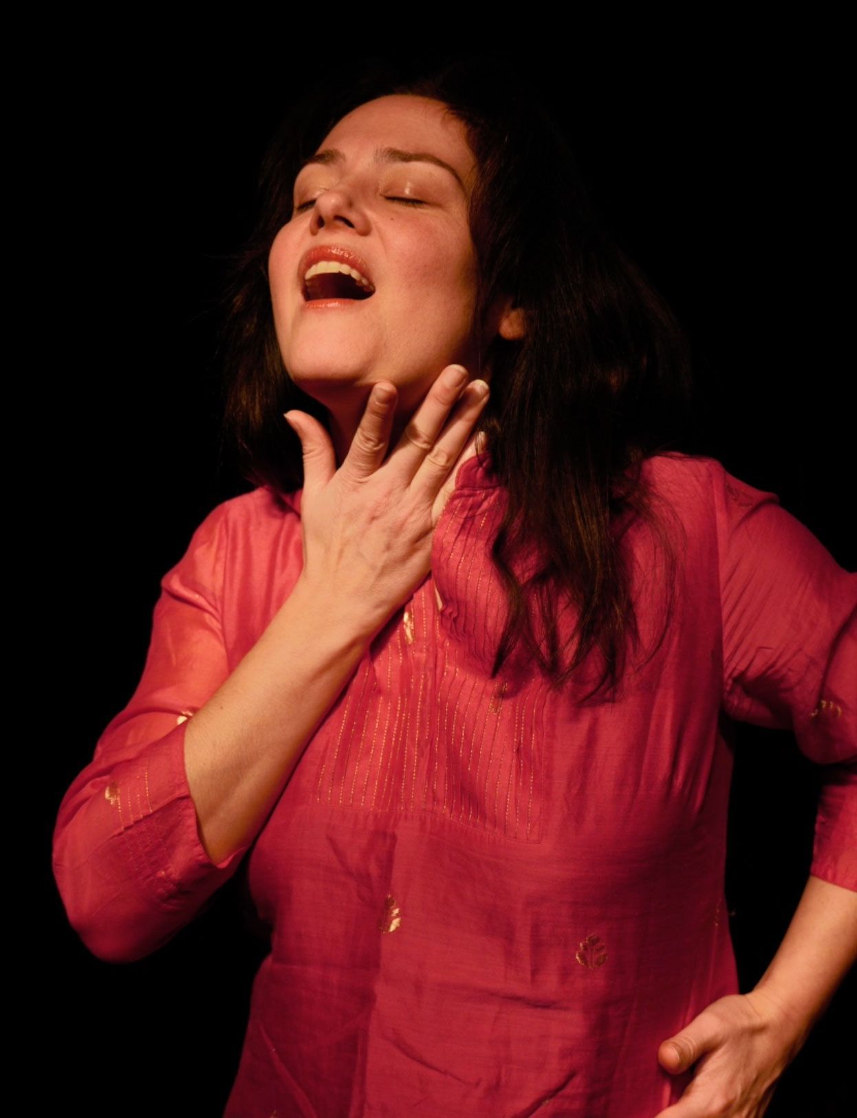 Une femme en chemise rose rit les yeux fermés