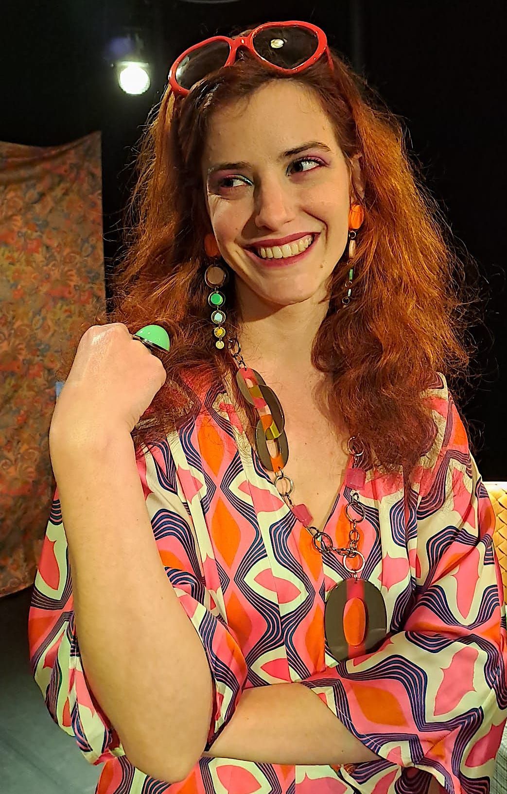 Une femme portant une robe colorée et des lunettes de soleil sourit.