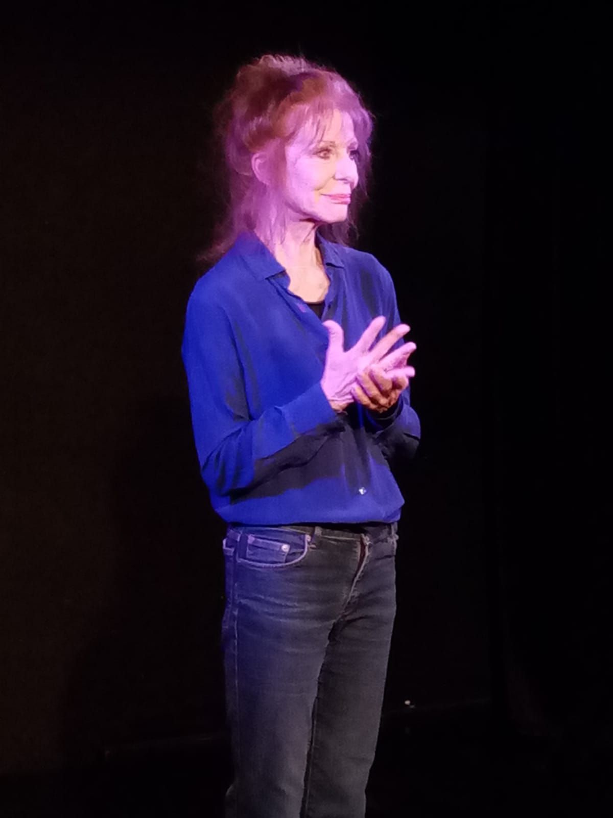 Une femme en chemise bleue et en jean tape dans ses mains sur une scène.