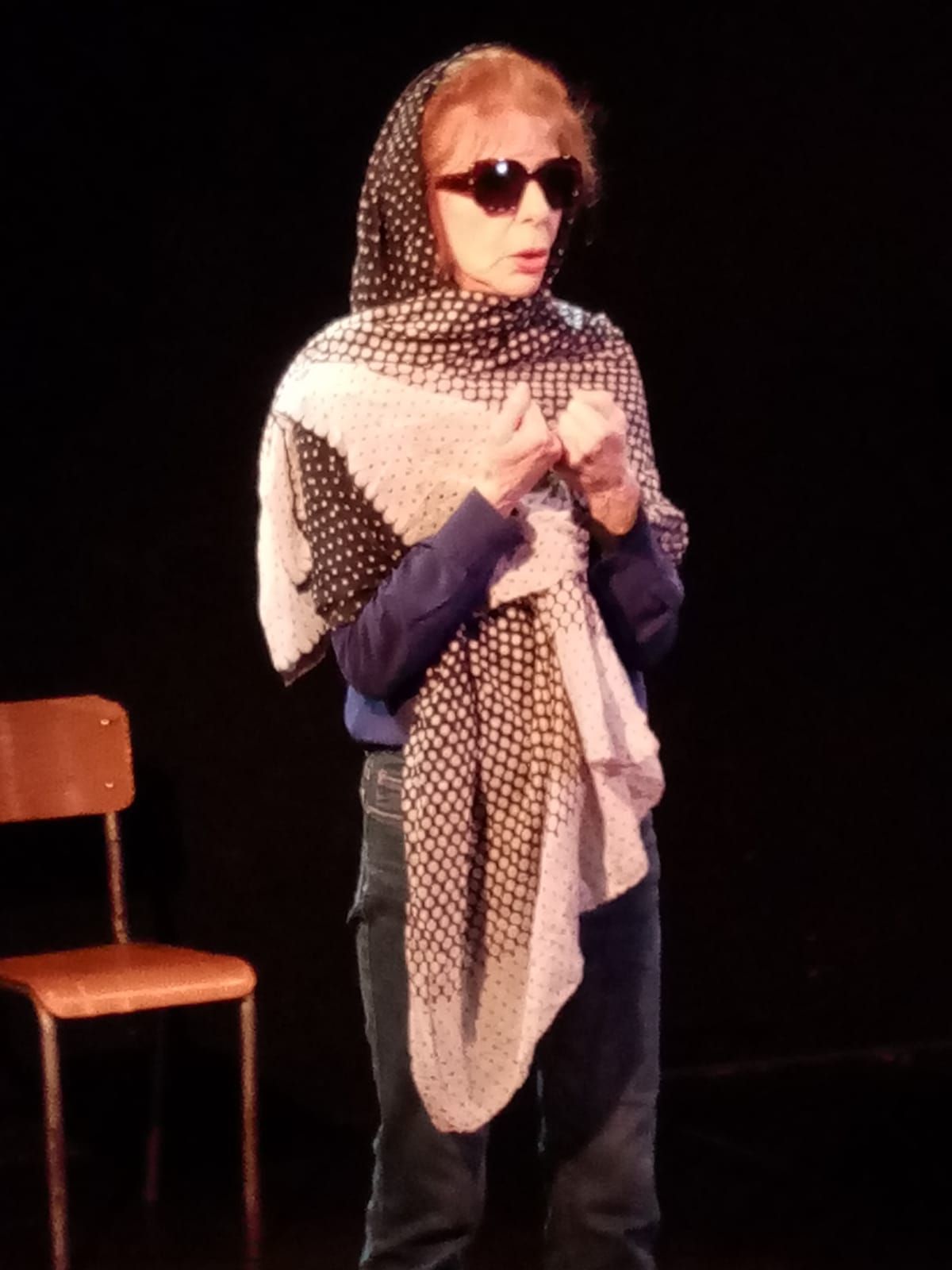Une femme portant des lunettes de soleil et un foulard se tient devant une chaise