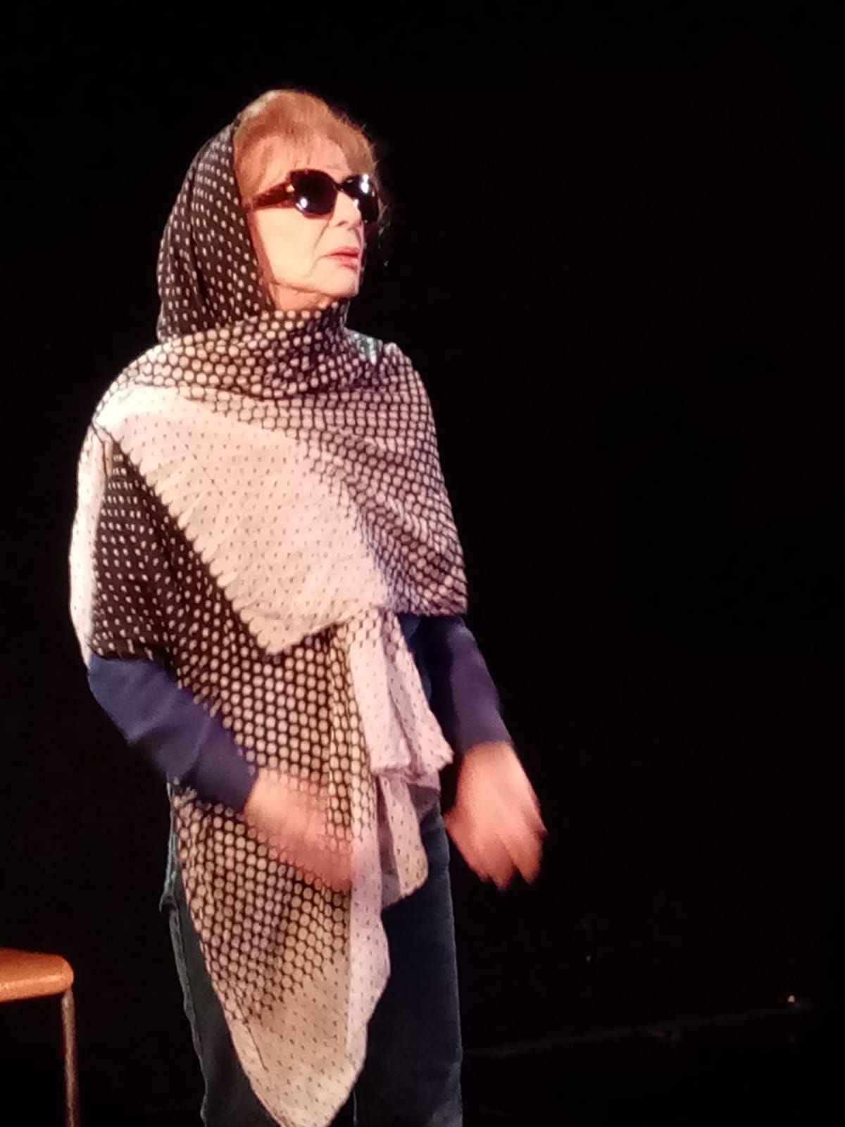 Une femme portant des lunettes de soleil et un foulard se tient dans le noir