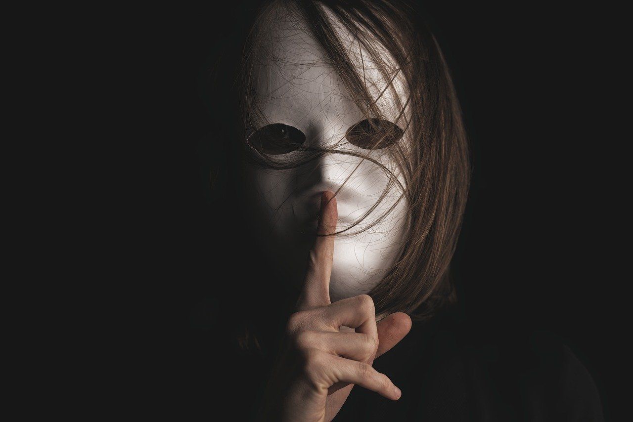 une femme portant un masque blanc fait un geste de silence