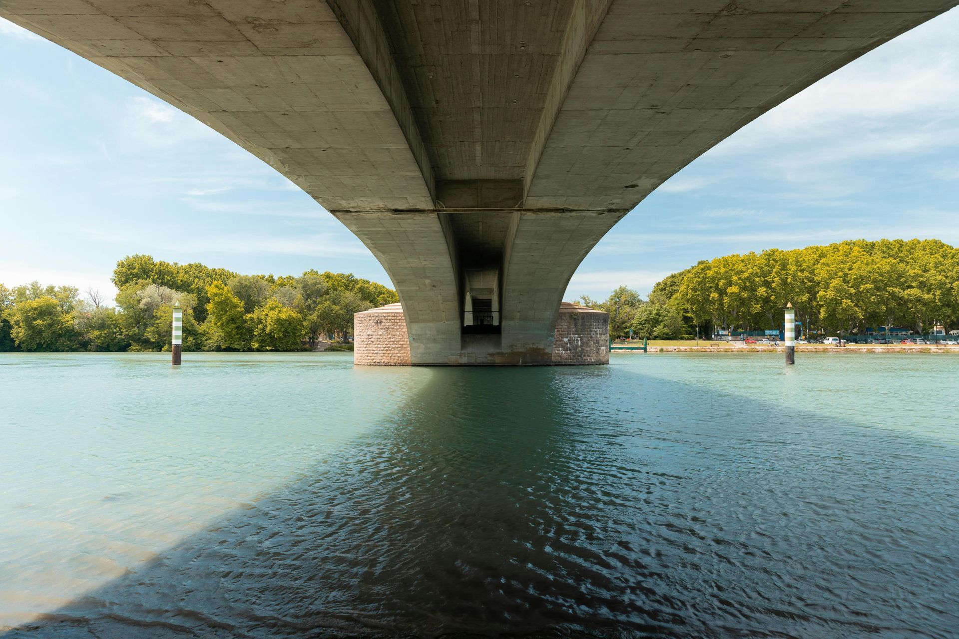 从阿维尼翁桥下眺望碧蓝的湖水。远处可见树木和天空。
