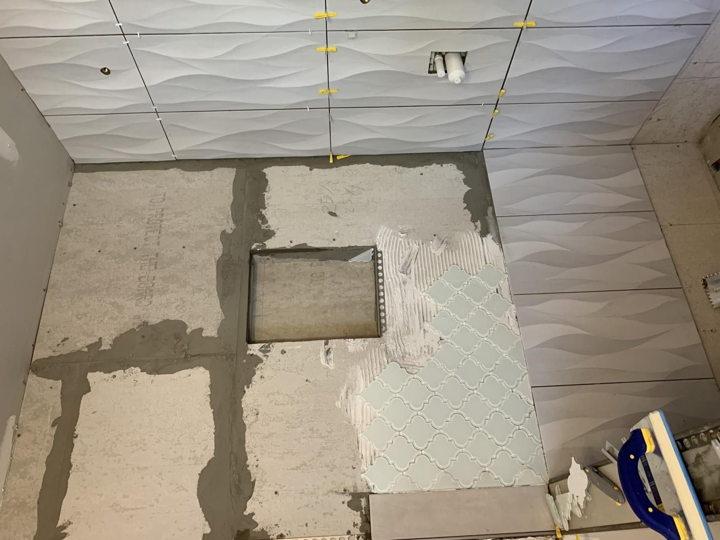 A bathroom with tiles being installed on the floor and walls.