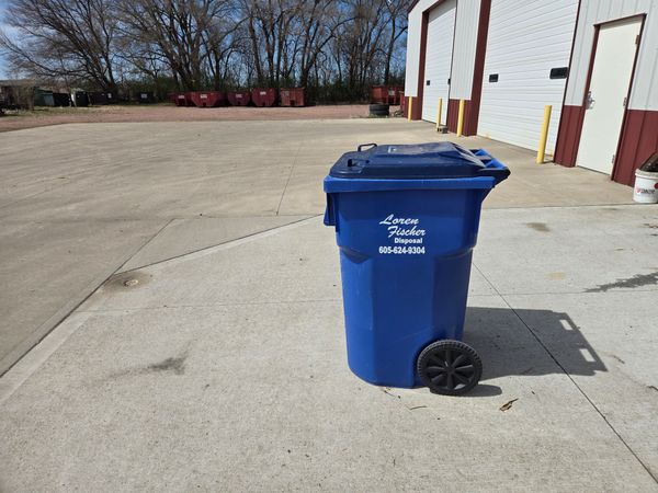 A row of colorful trash and recycling bins sits on a concrete ledge against a gray building wall.