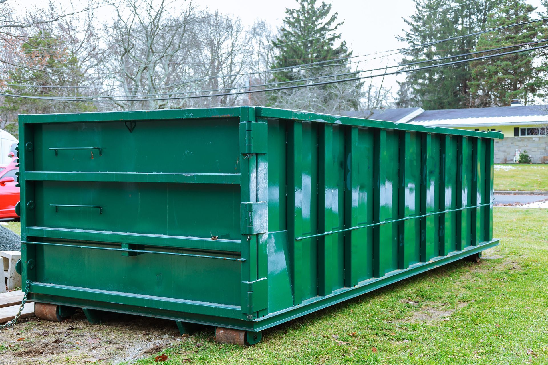 A large, empty rectangular green metal roll-off dumpster sitting on a grassy lawn.