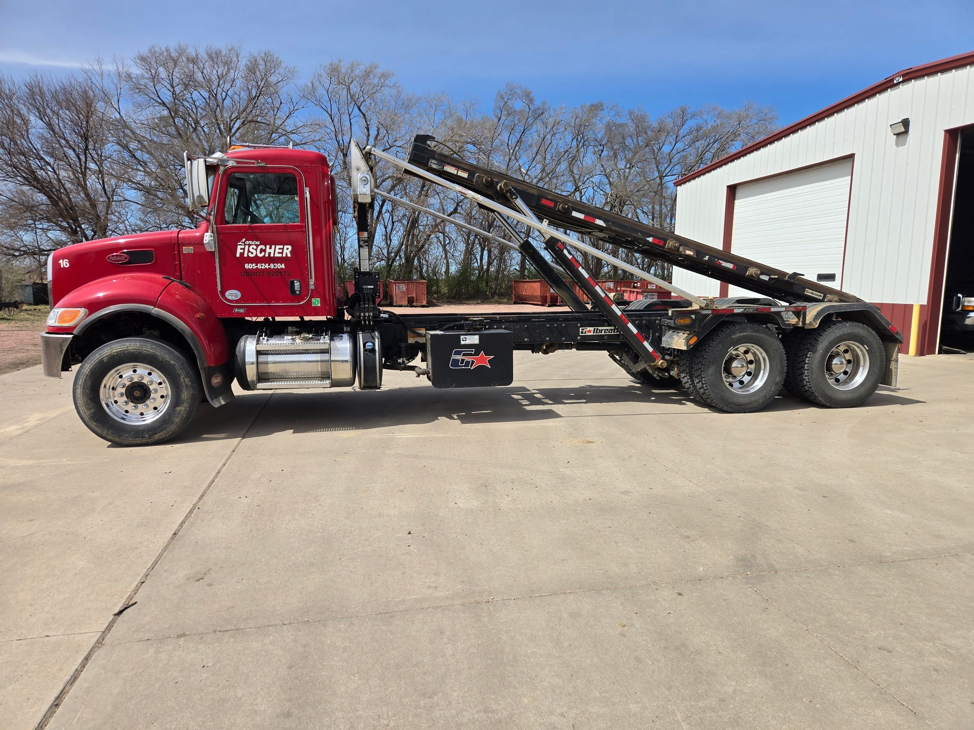 A green garbage truck driving on an asphalt road seen from an elevated angle.