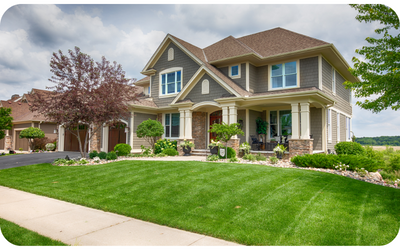 Two-story house with green lawn, beige trim, and brown roof. Front porch, side garage, and cloudy sky.