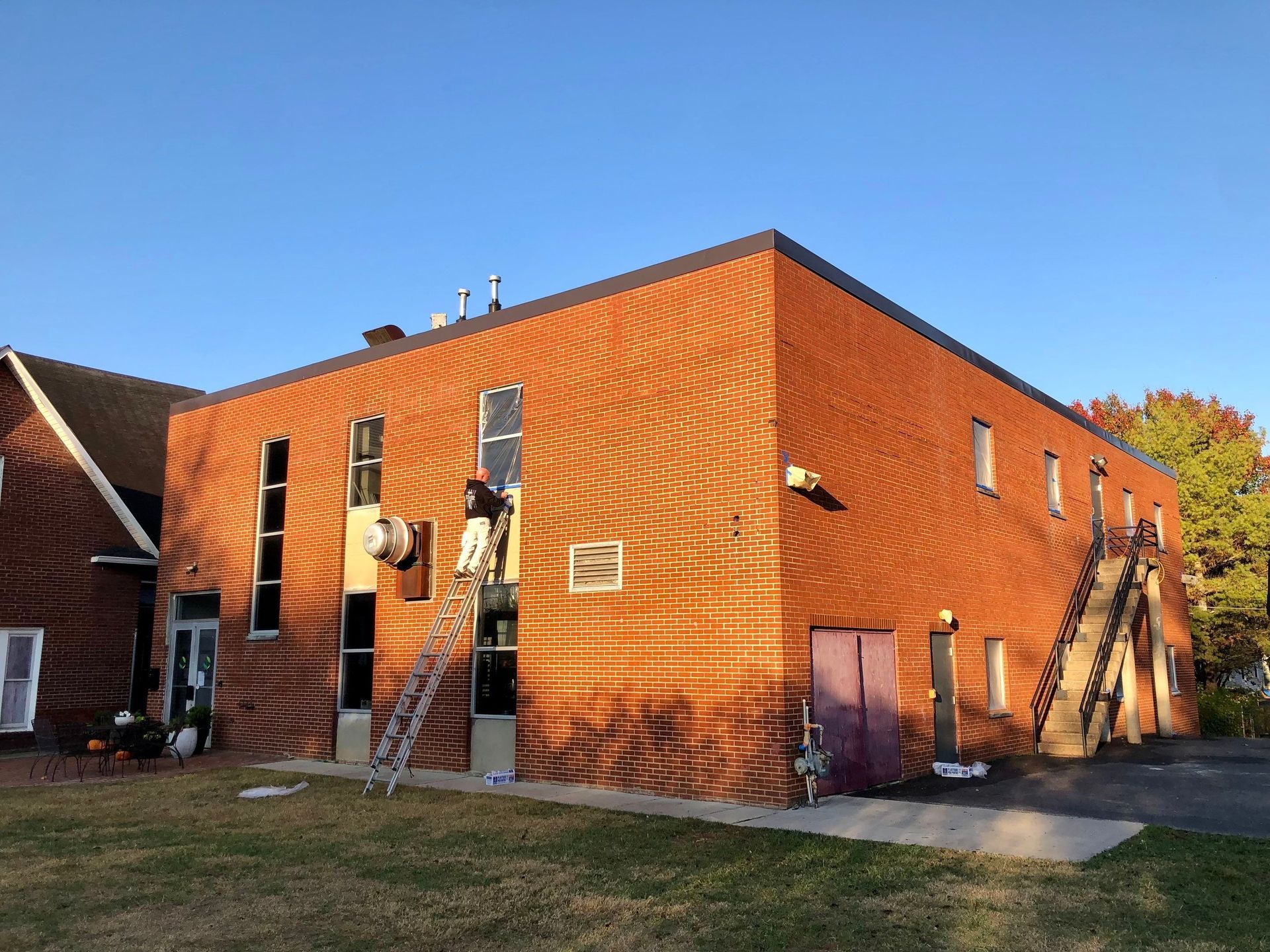 A man is standing on a ladder on the side of a brick building.