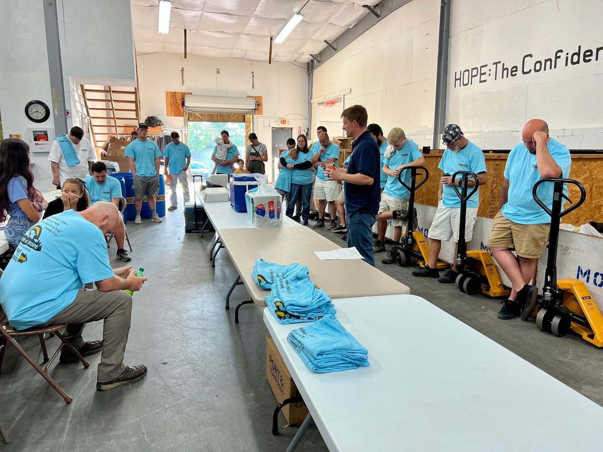 A group of people in blue shirts are standing around tables in a room.