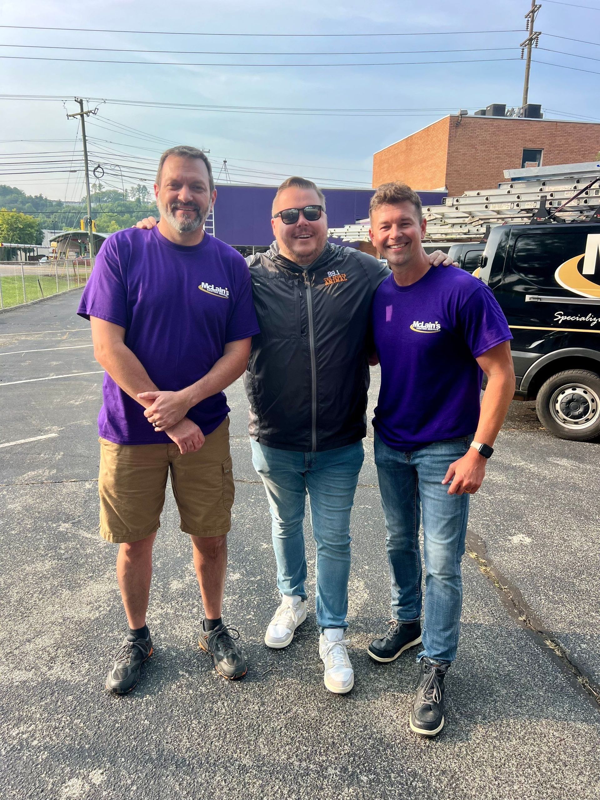 Three men in purple shirts are posing for a picture in a parking lot.