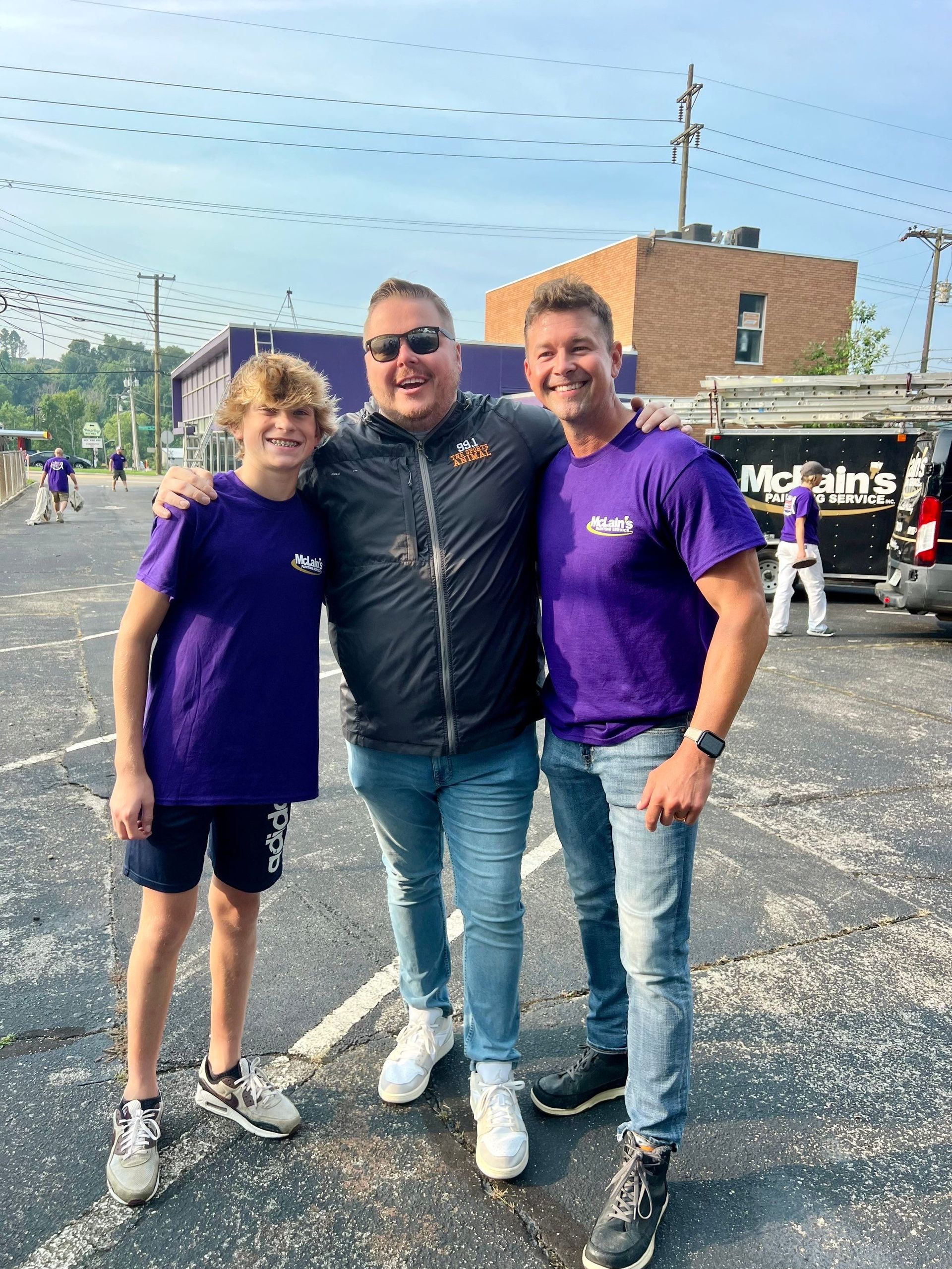 Three men are posing for a picture in a parking lot.