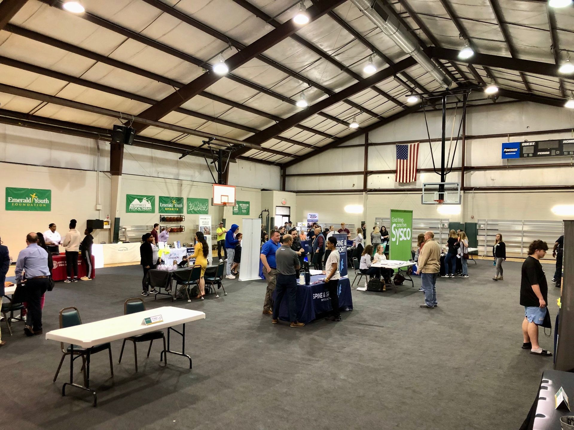 A group of people are standing around tables in a large room.