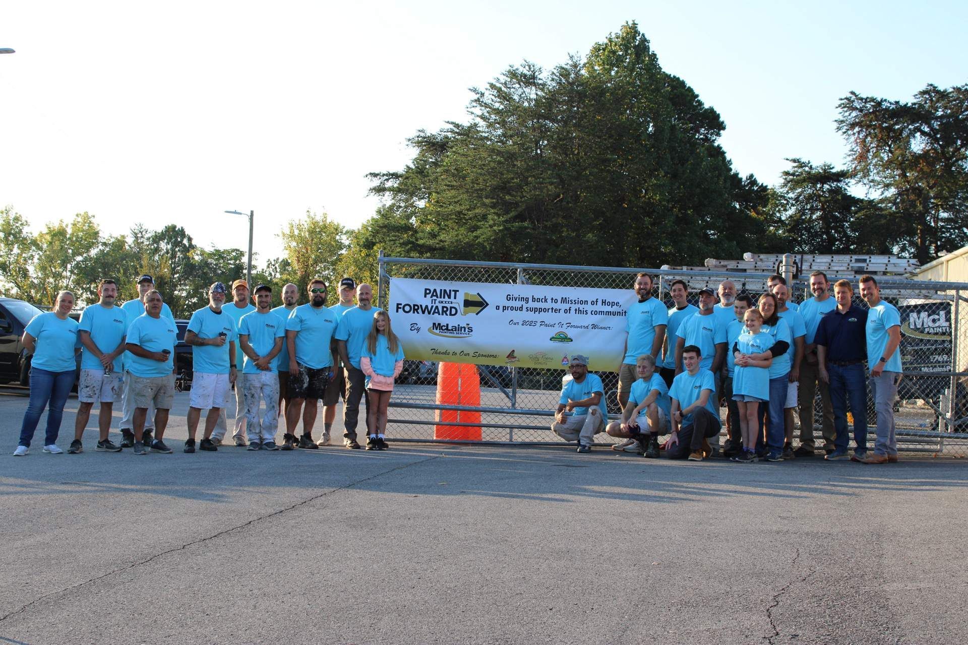 A group of people are posing for a picture in front of a sign that says helping