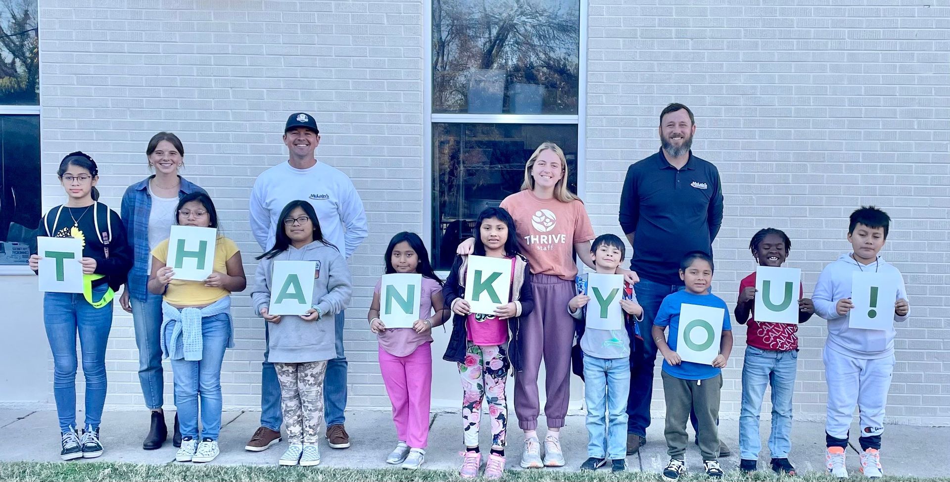 A group of people are standing in front of a building holding signs that say `` thank you ''.