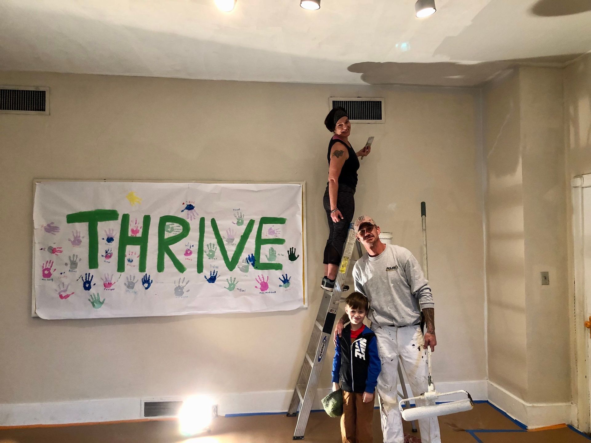 A family is painting a room with a banner that says thrive.