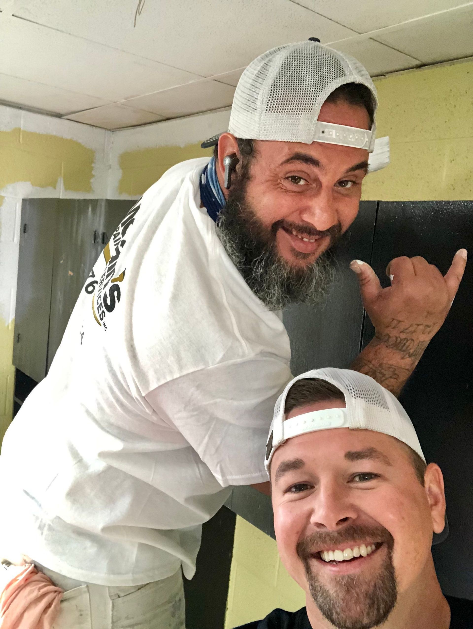 Two men are posing for a picture and one is wearing a white hat