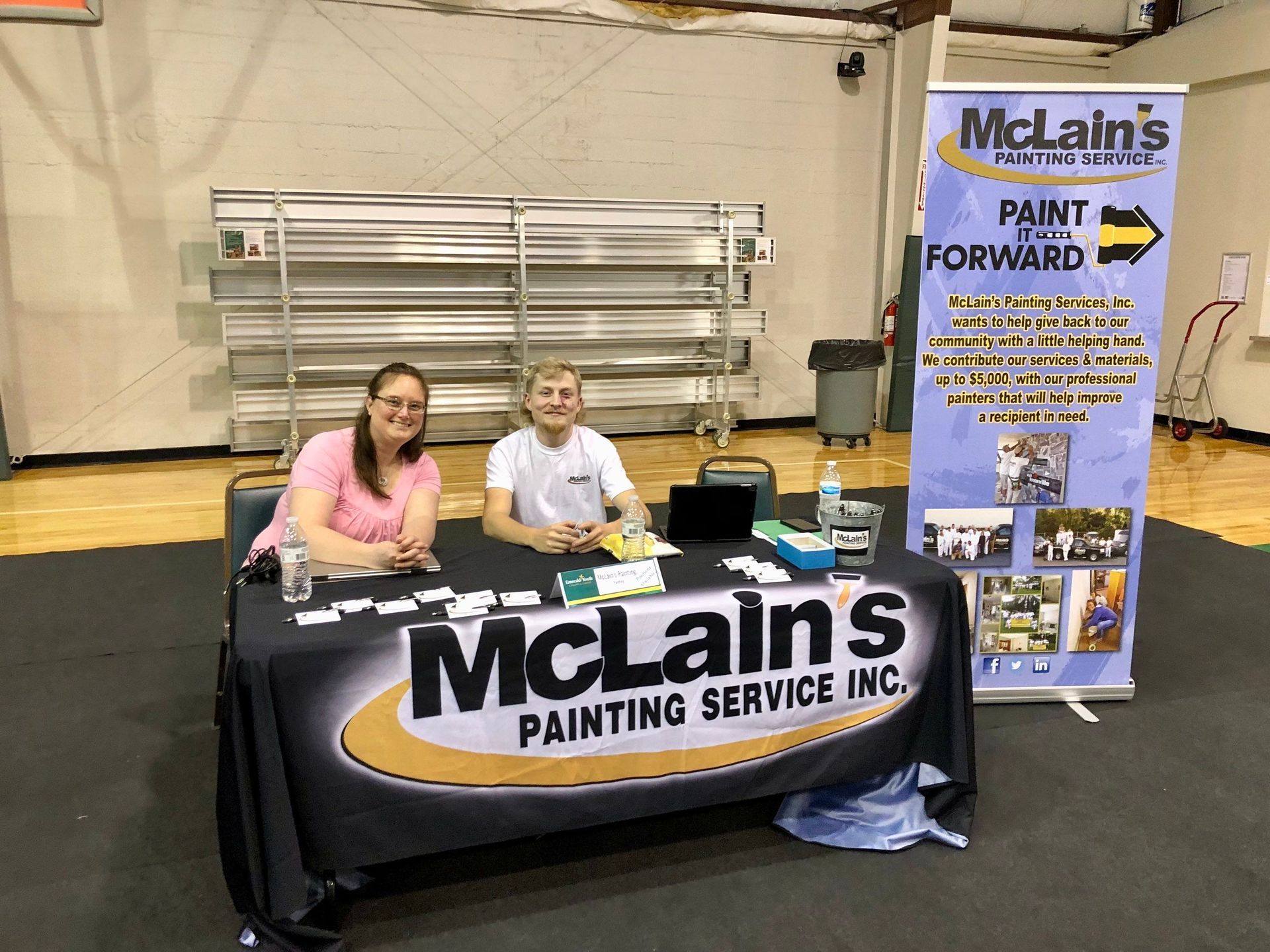 Two people are sitting at a table with a sign that says mclain 's painting service inc.