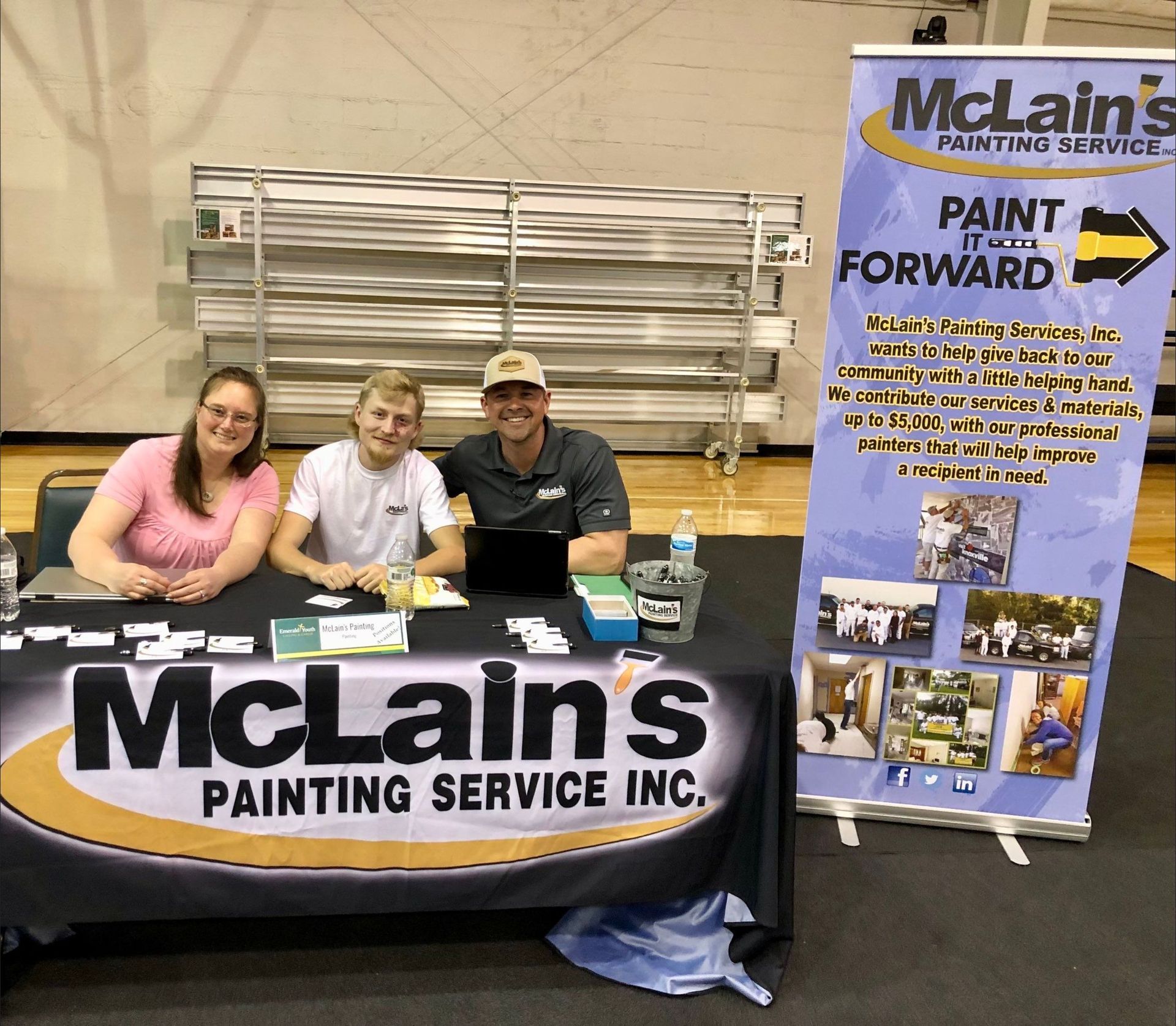 A group of people are sitting at a table with a sign that says mclain 's painting service inc.