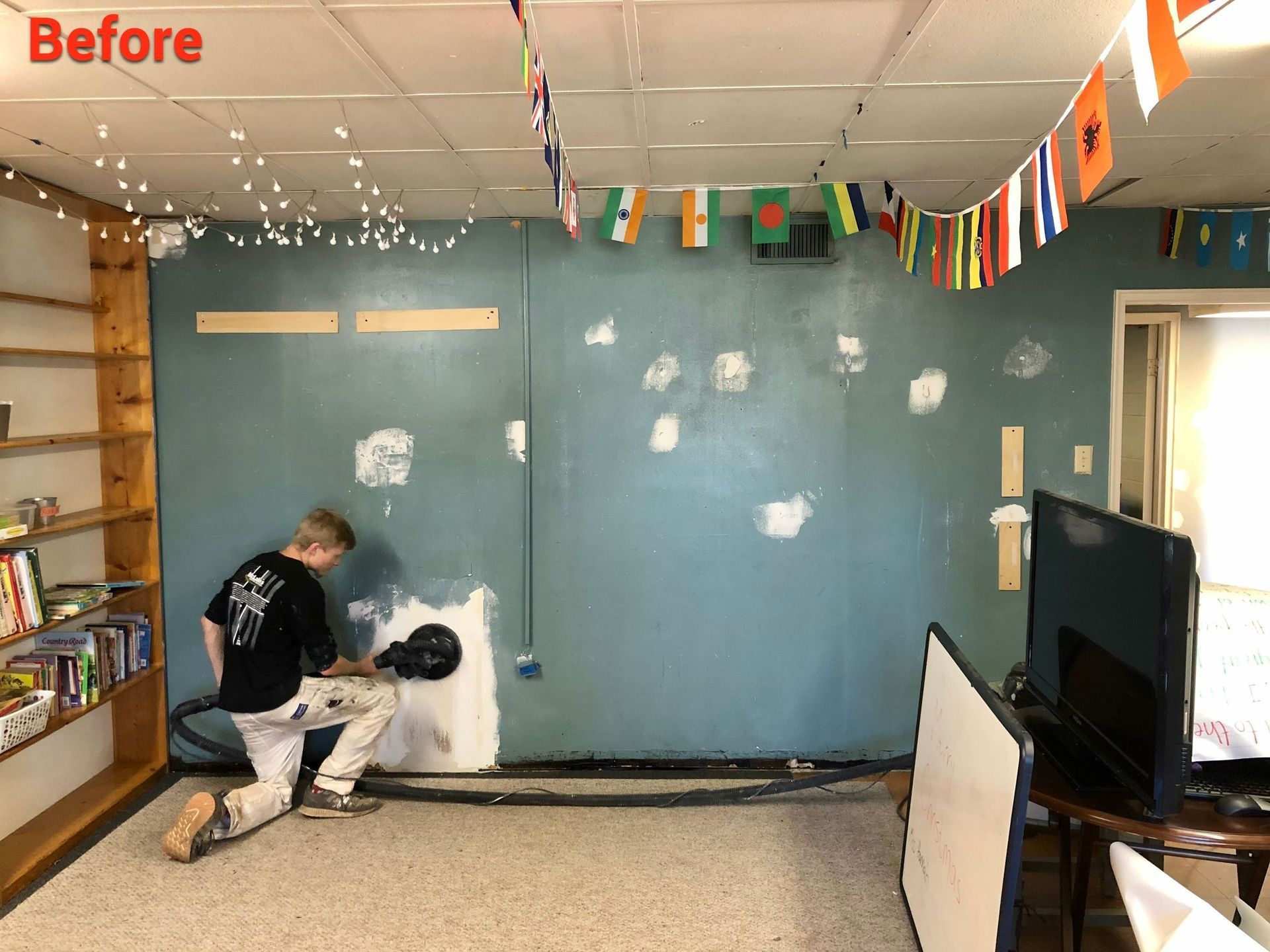 A man is painting a wall in a room with flags hanging from the ceiling.