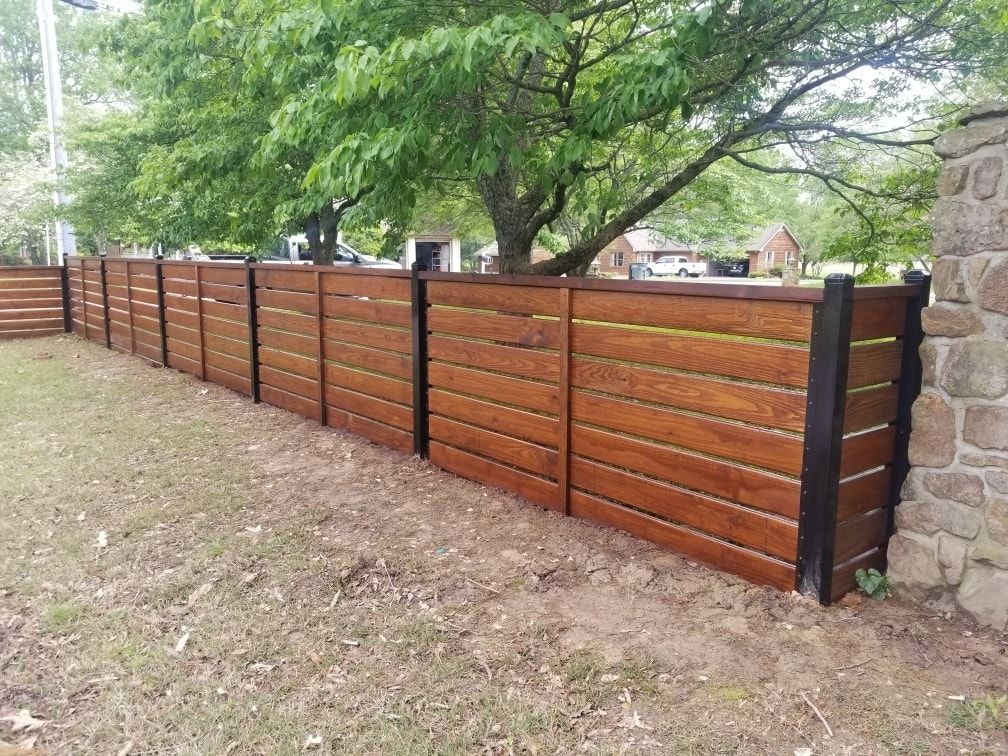 A wooden fence is surrounded by trees and a stone wall.