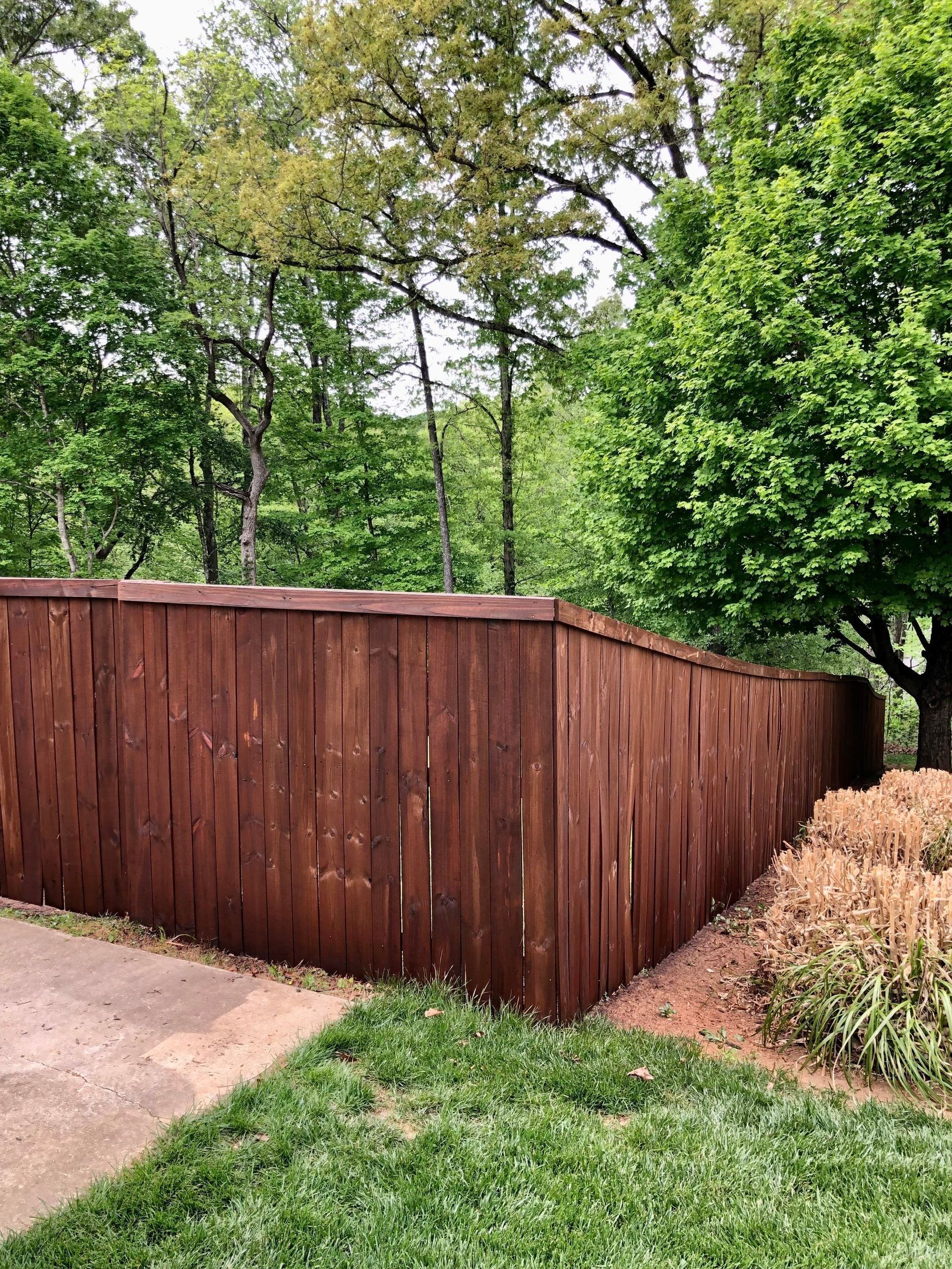 A wooden fence is surrounded by trees and grass in a yard.