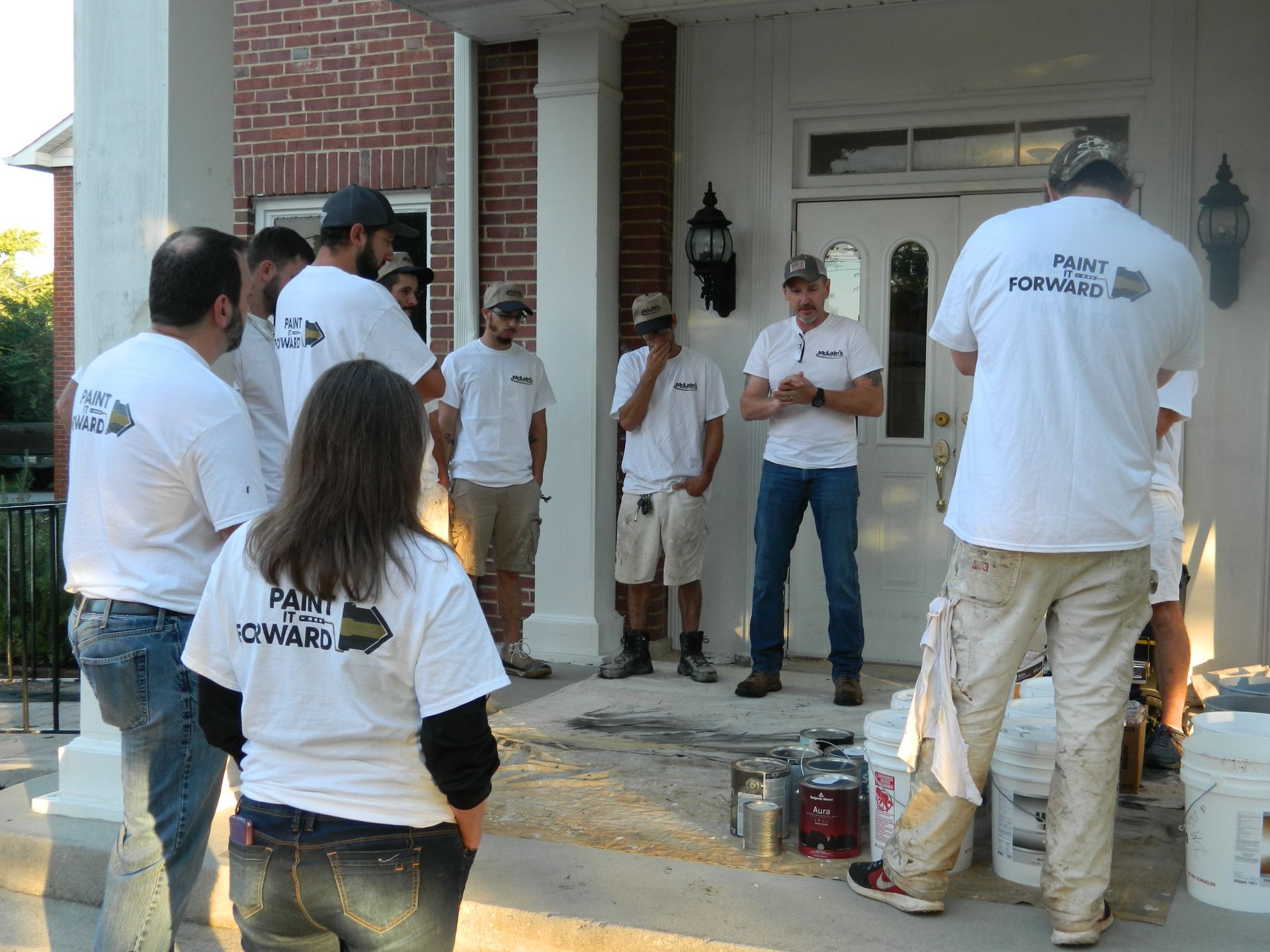 A group of people standing in front of a house with one wearing a shirt that says 