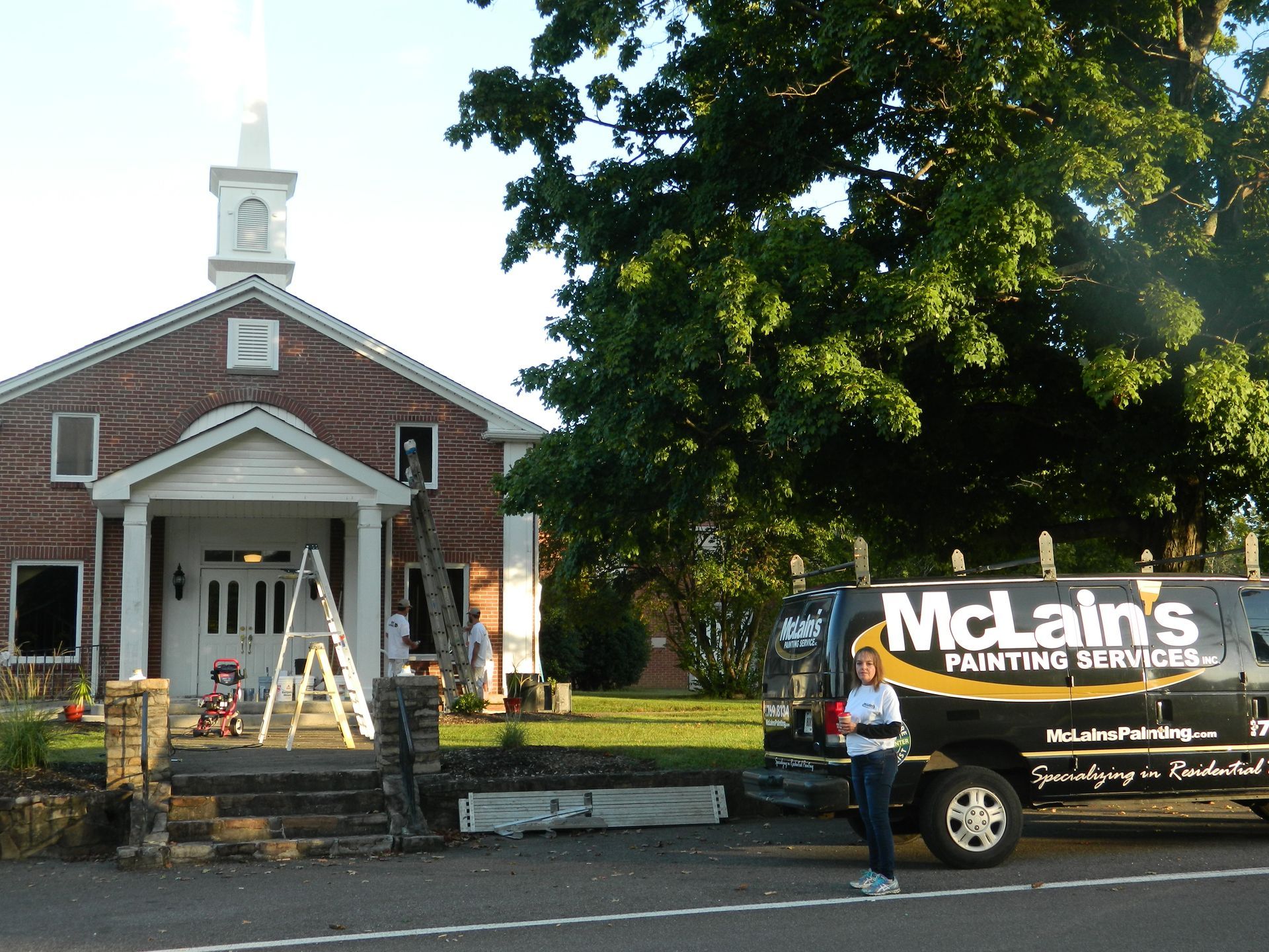 A mclain 's painting service truck is parked in front of a church
