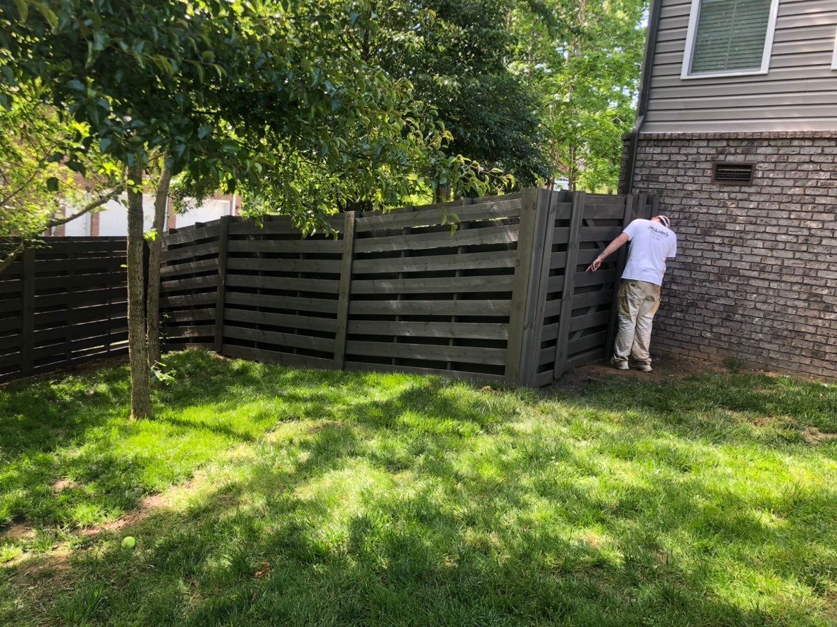 A man is standing next to a wooden fence in a backyard.