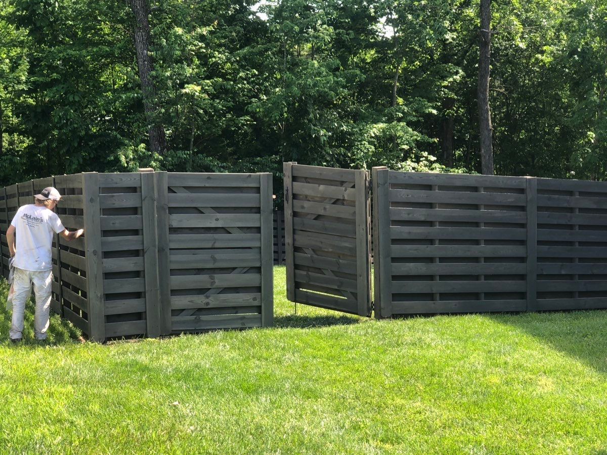 A man is standing in front of a wooden fence in a grassy field.