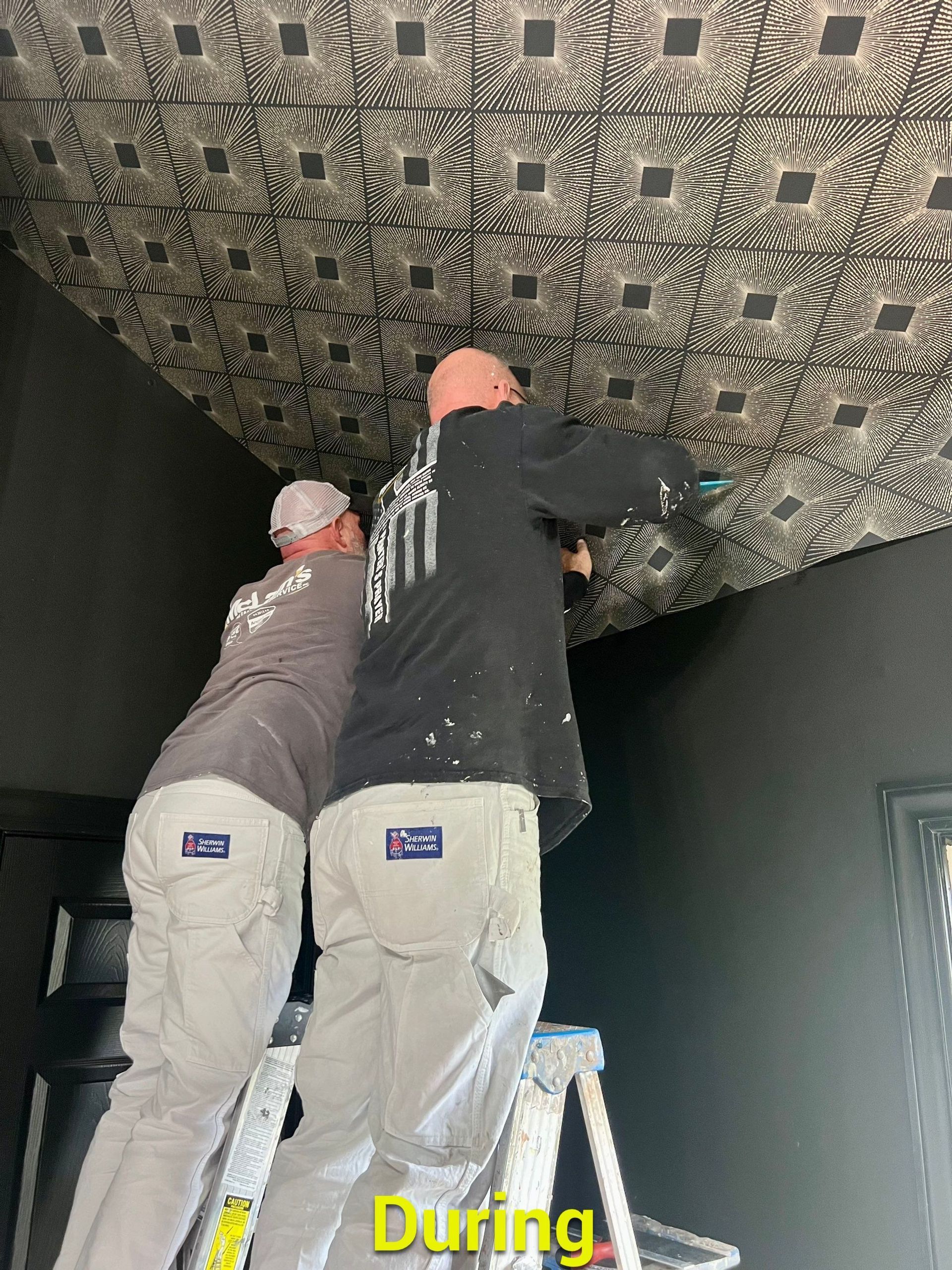 Two men are standing on a ladder working on a ceiling.