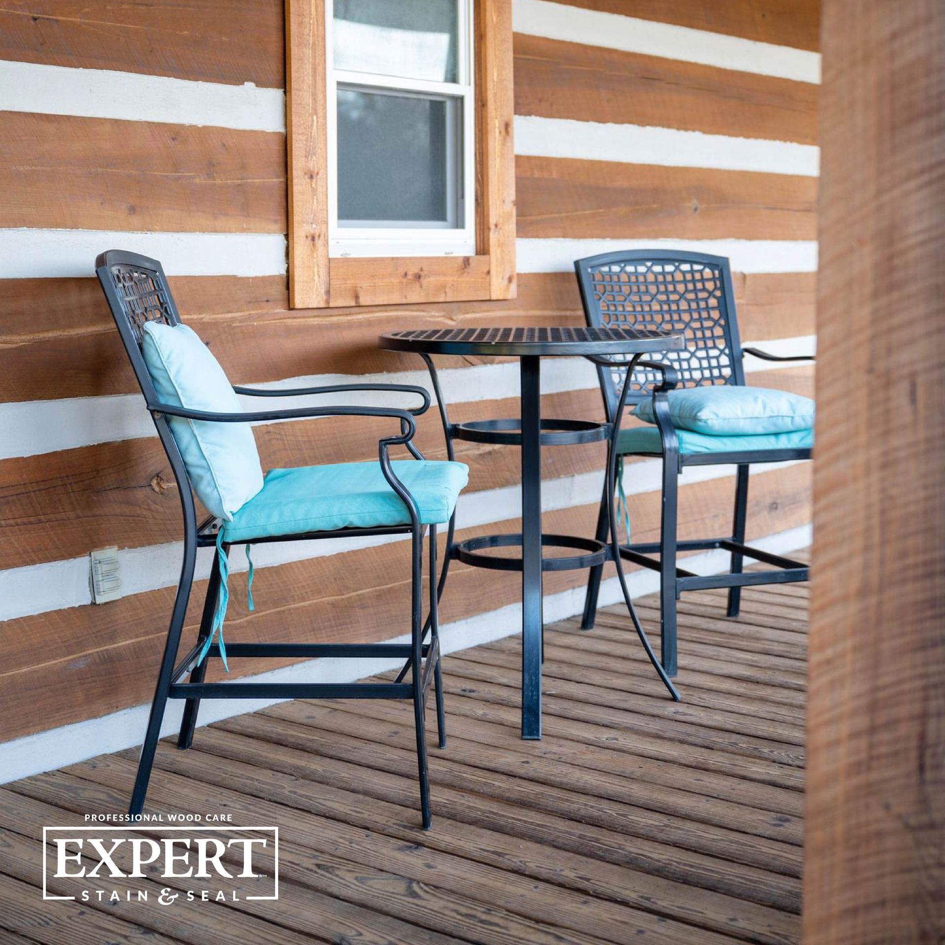 A wooden porch with a table and chairs in front of a log cabin.