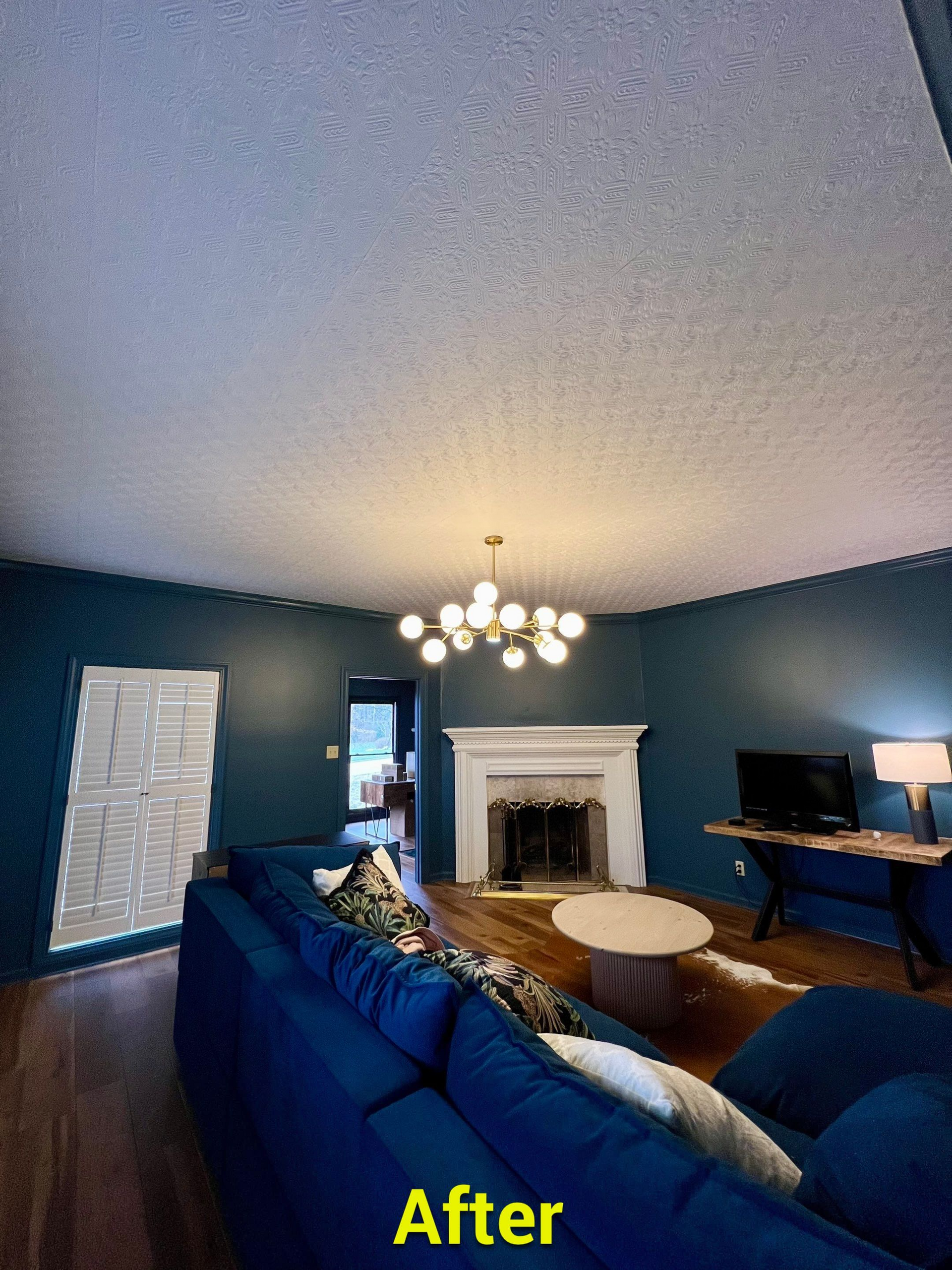 A living room with blue walls , a blue couch , a fireplace and a chandelier.