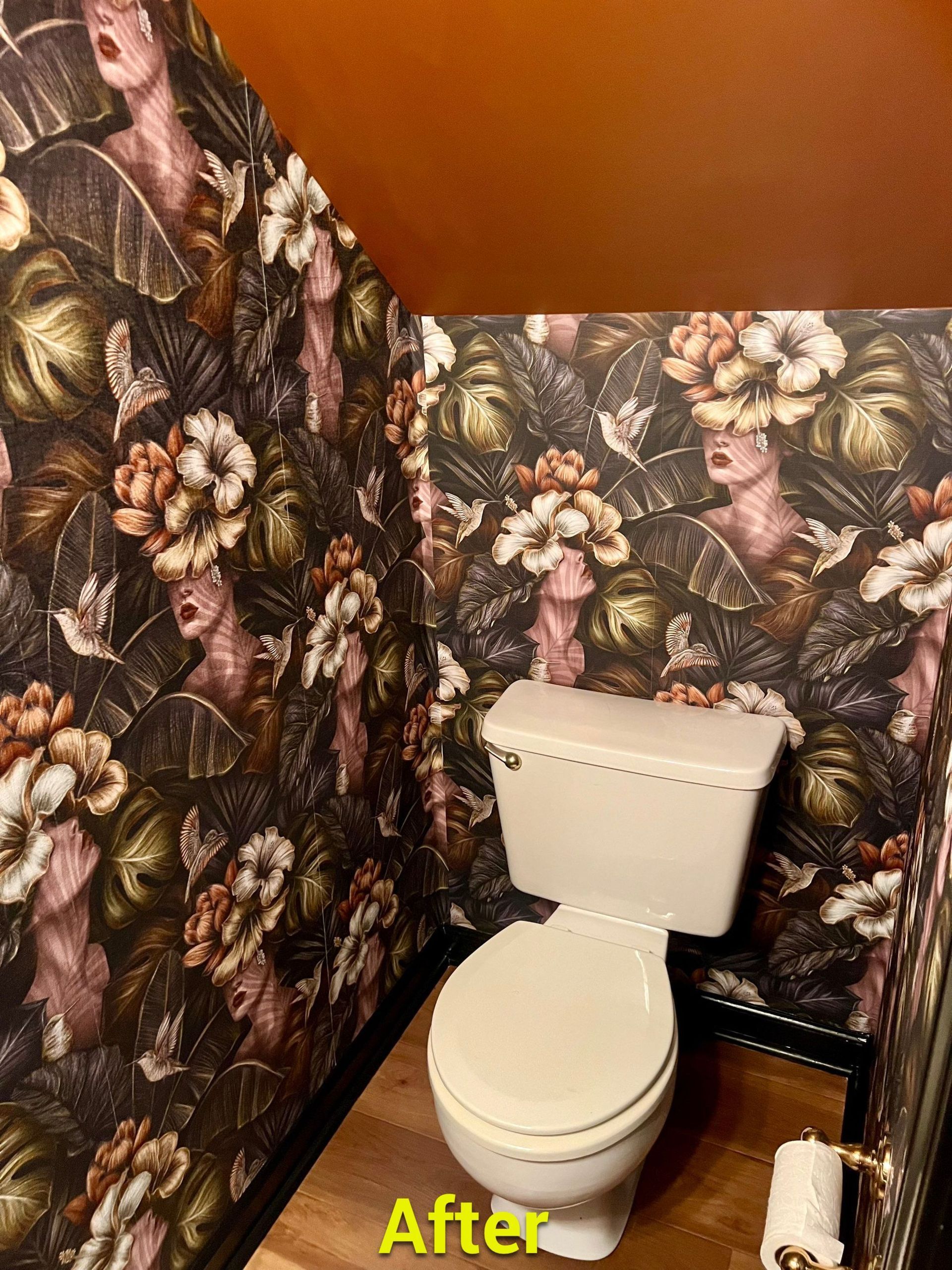 A toilet in a bathroom with a floral wallpaper on the wall.