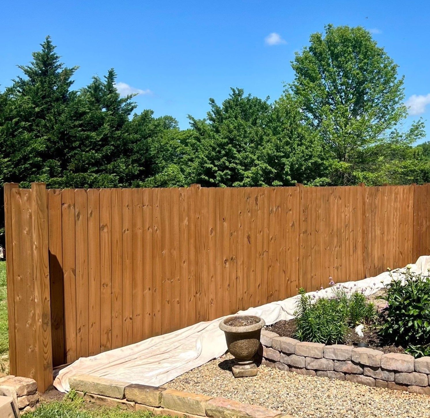 A wooden fence surrounds a garden with trees in the background