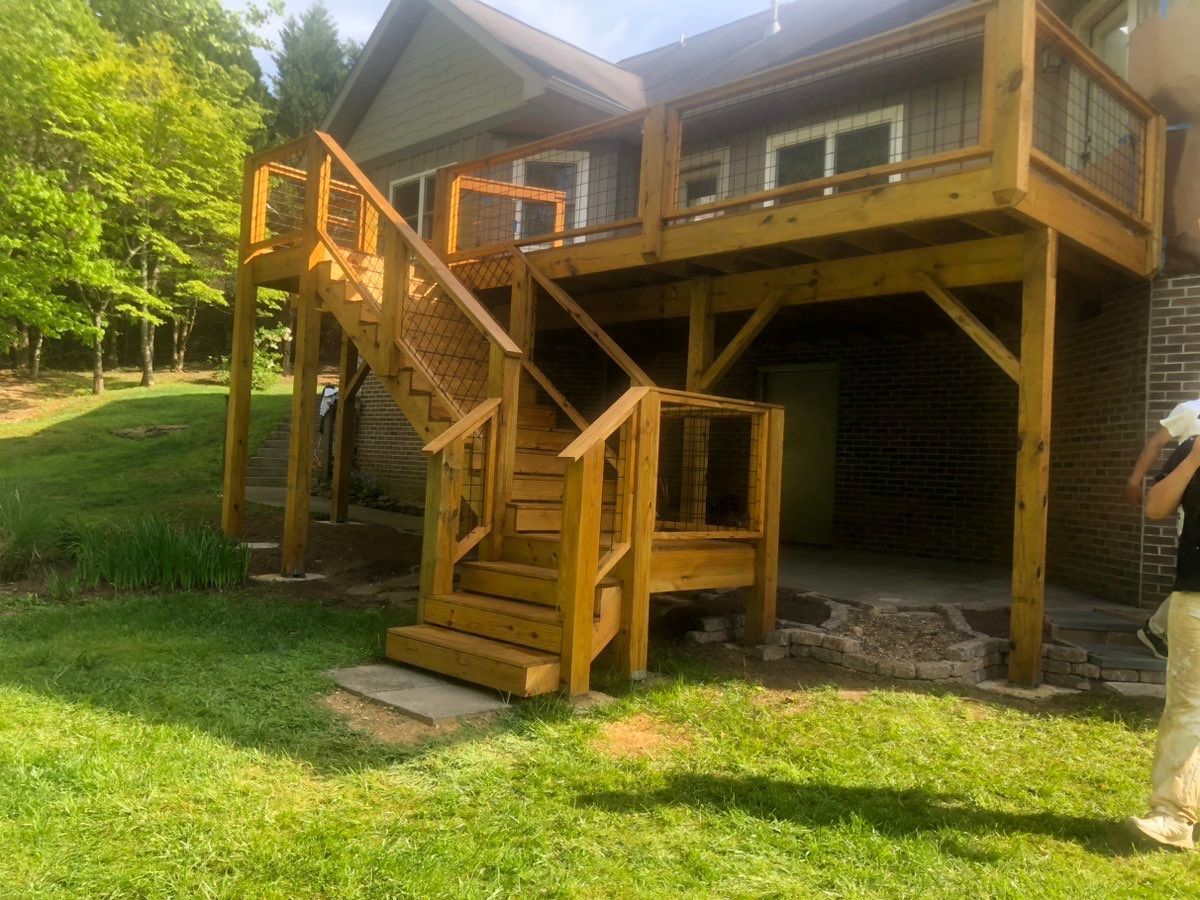 A woman is walking in front of a house with a wooden deck and stairs.