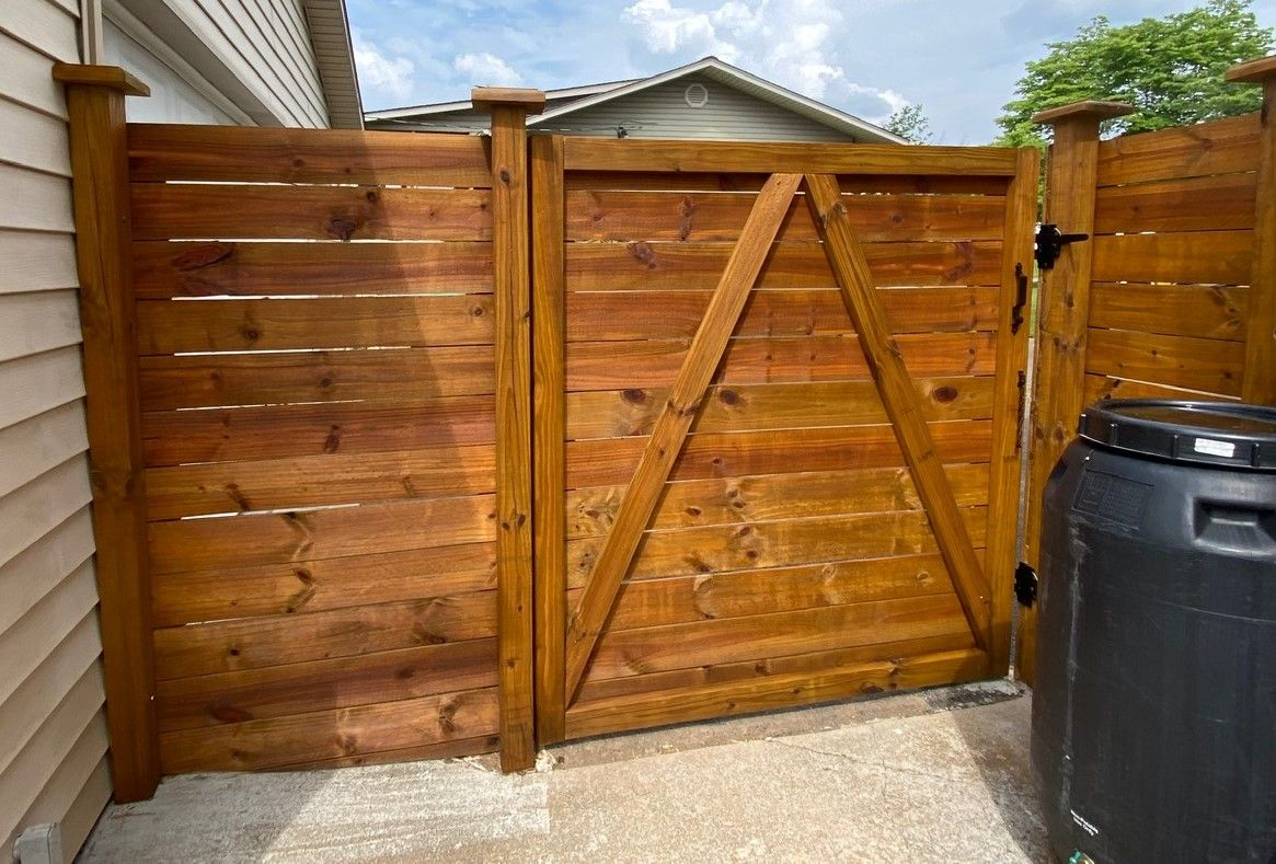 A wooden fence with a black trash can in front of it.