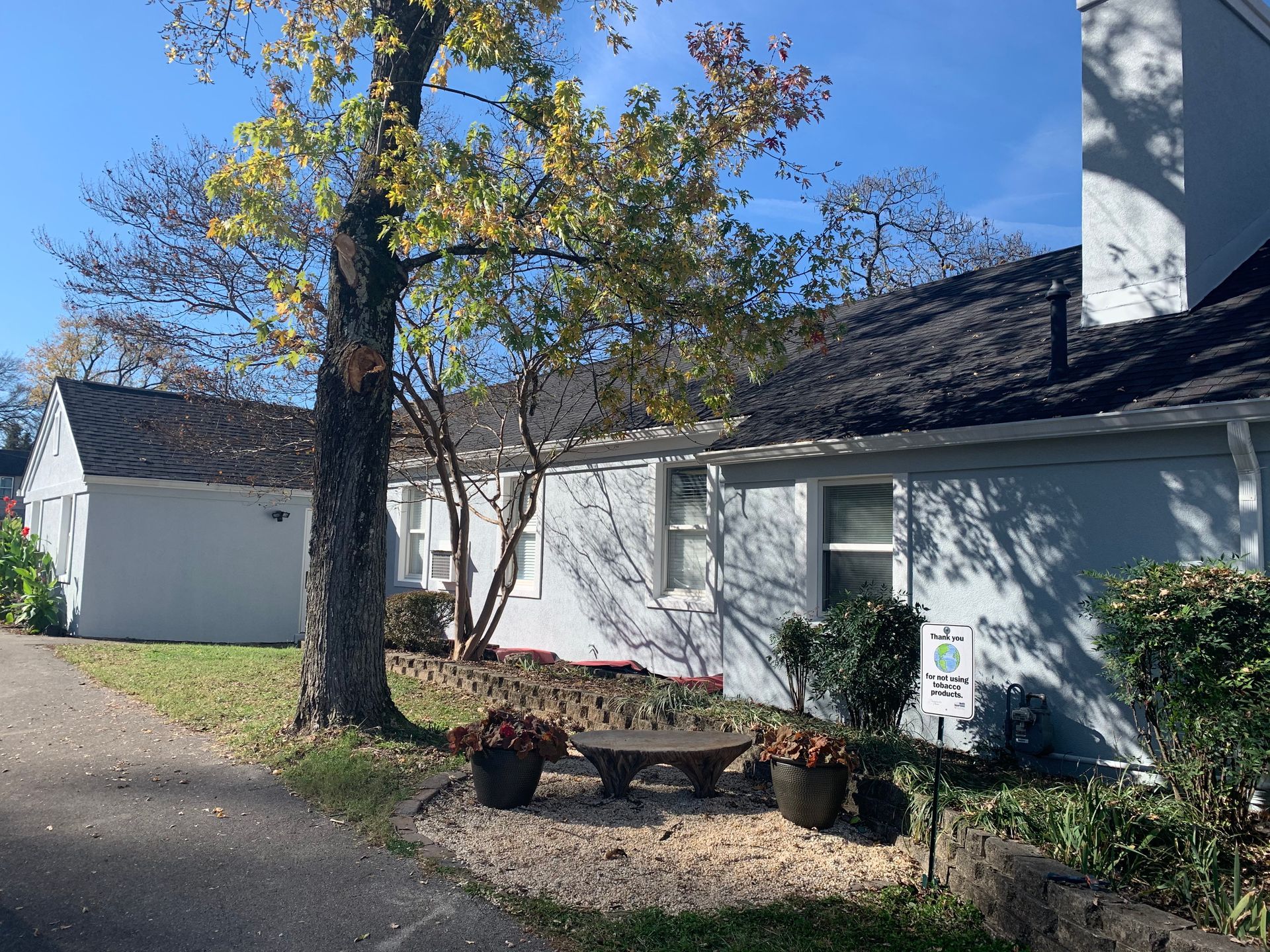 A white house with a black roof and a tree in front of it