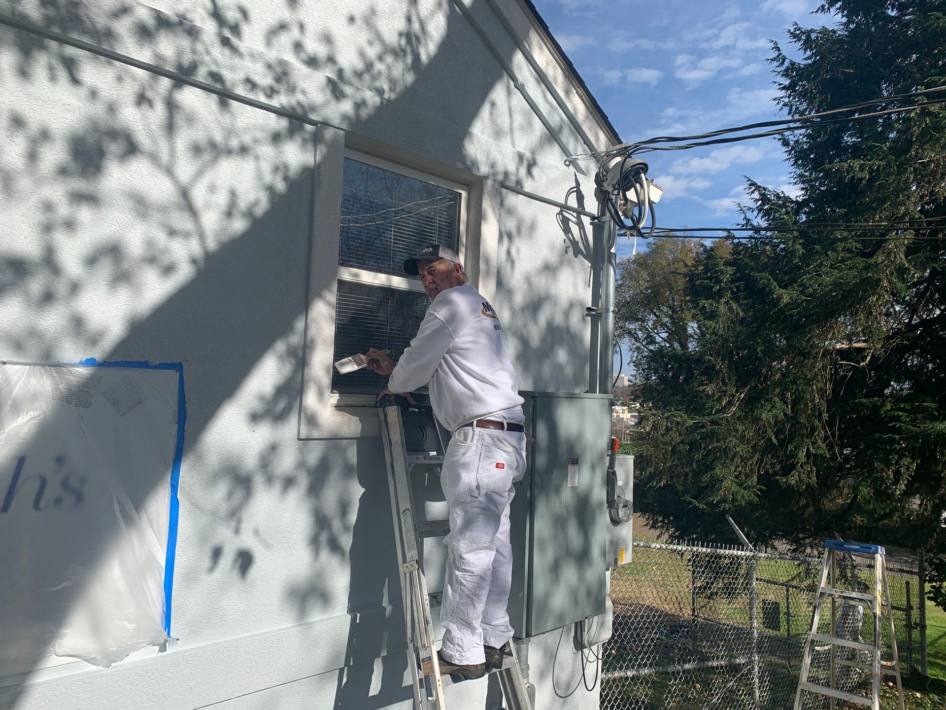 A man is standing on a ladder painting a house.