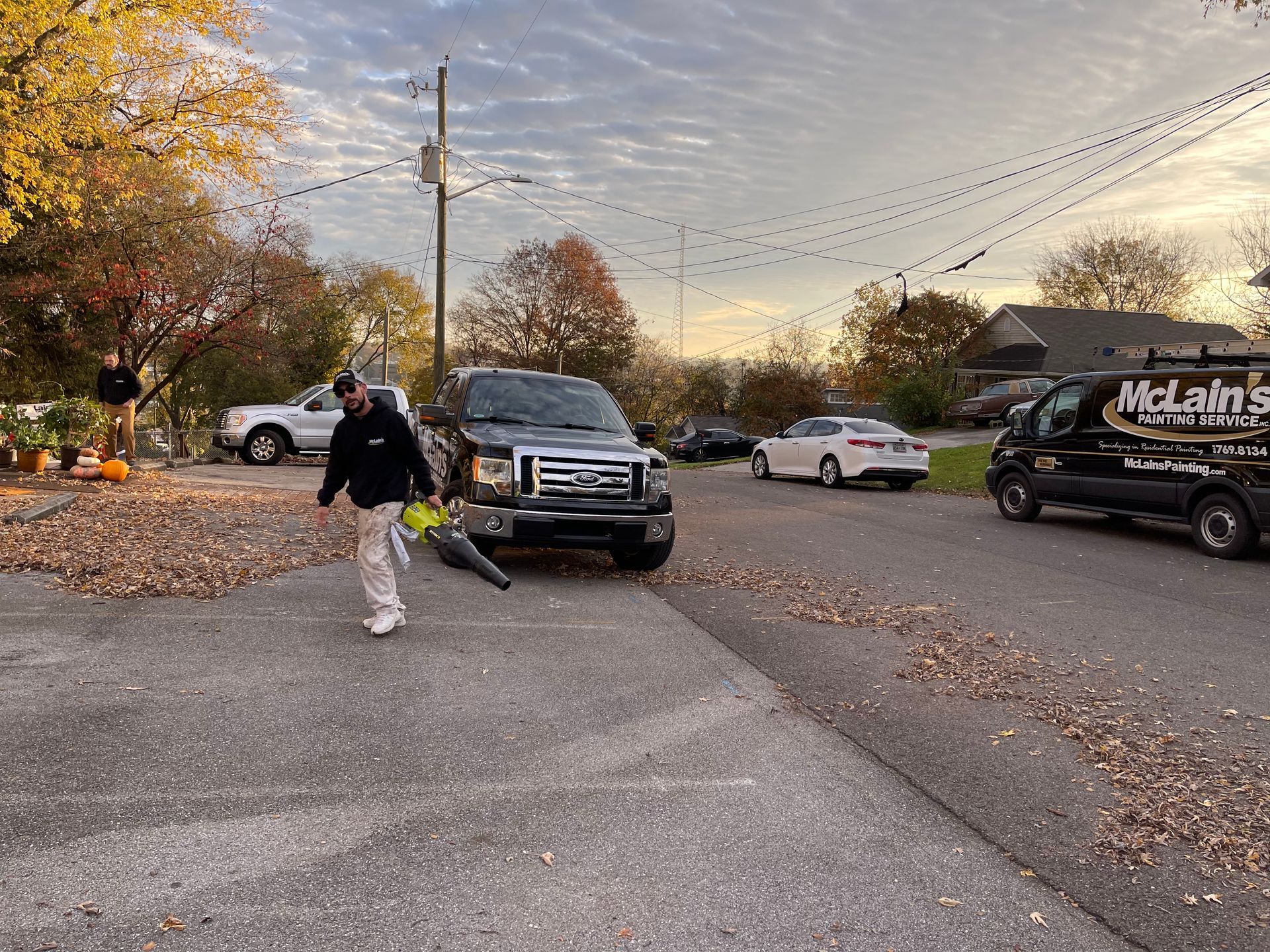 A man is blowing leaves in a parking lot next to a truck.