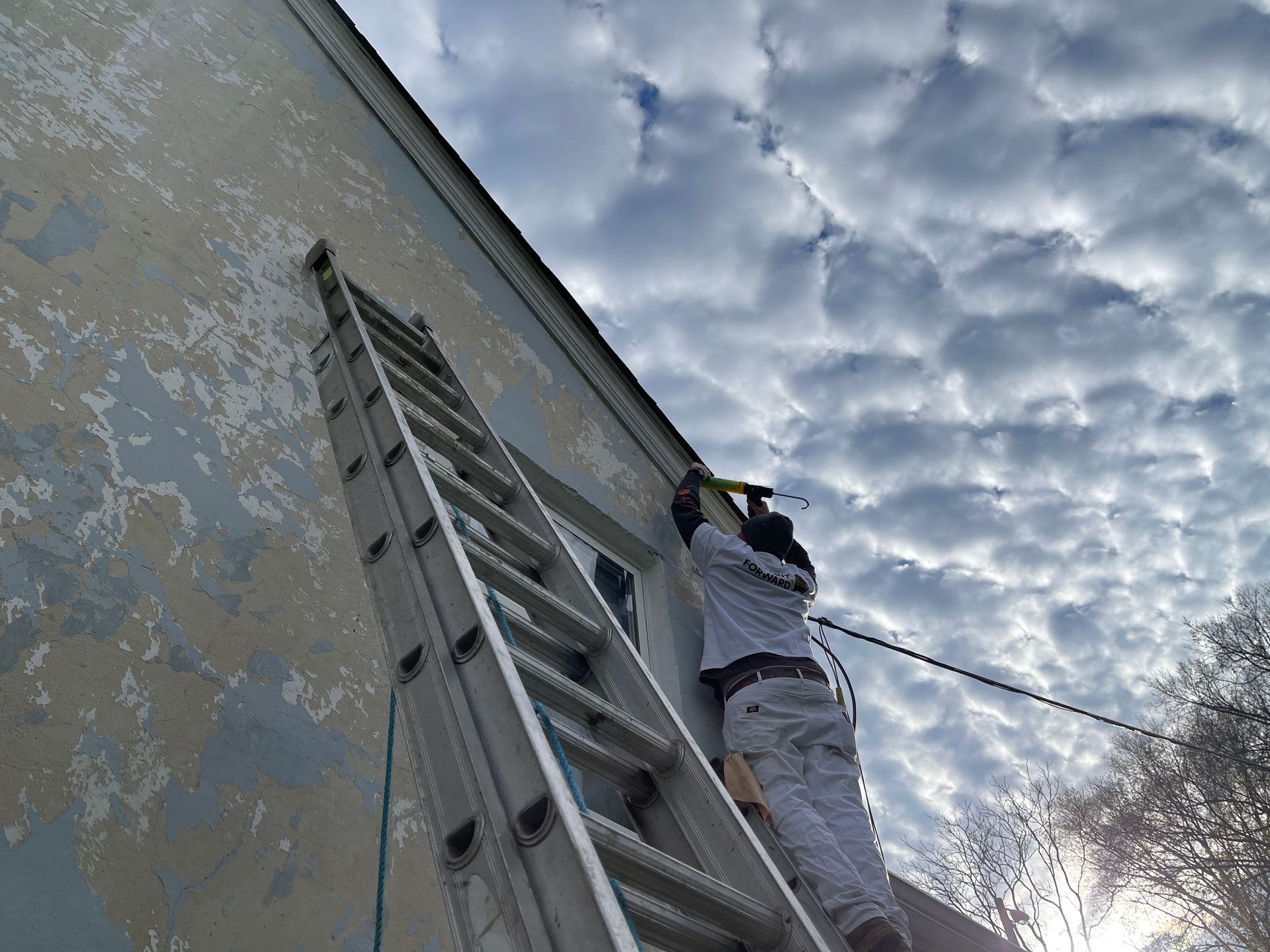 A man is climbing up a ladder to paint a building.