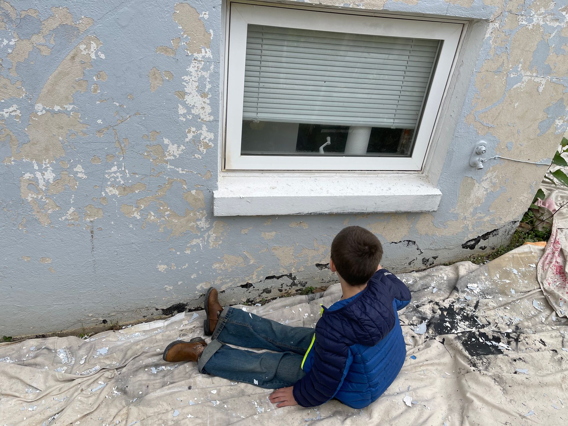 A young boy is sitting on the ground looking out a window.