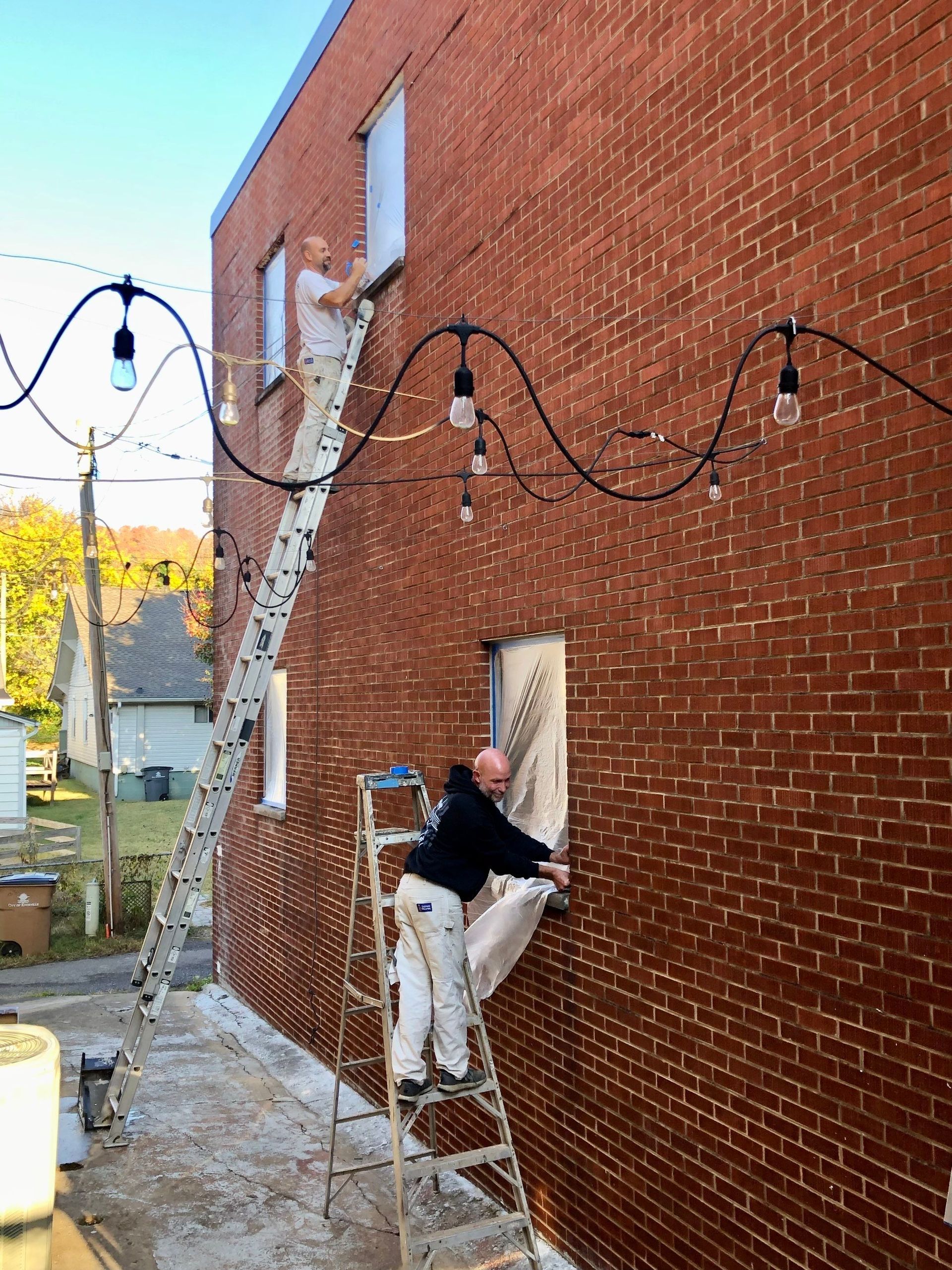 Two men are painting a brick building with a ladder.